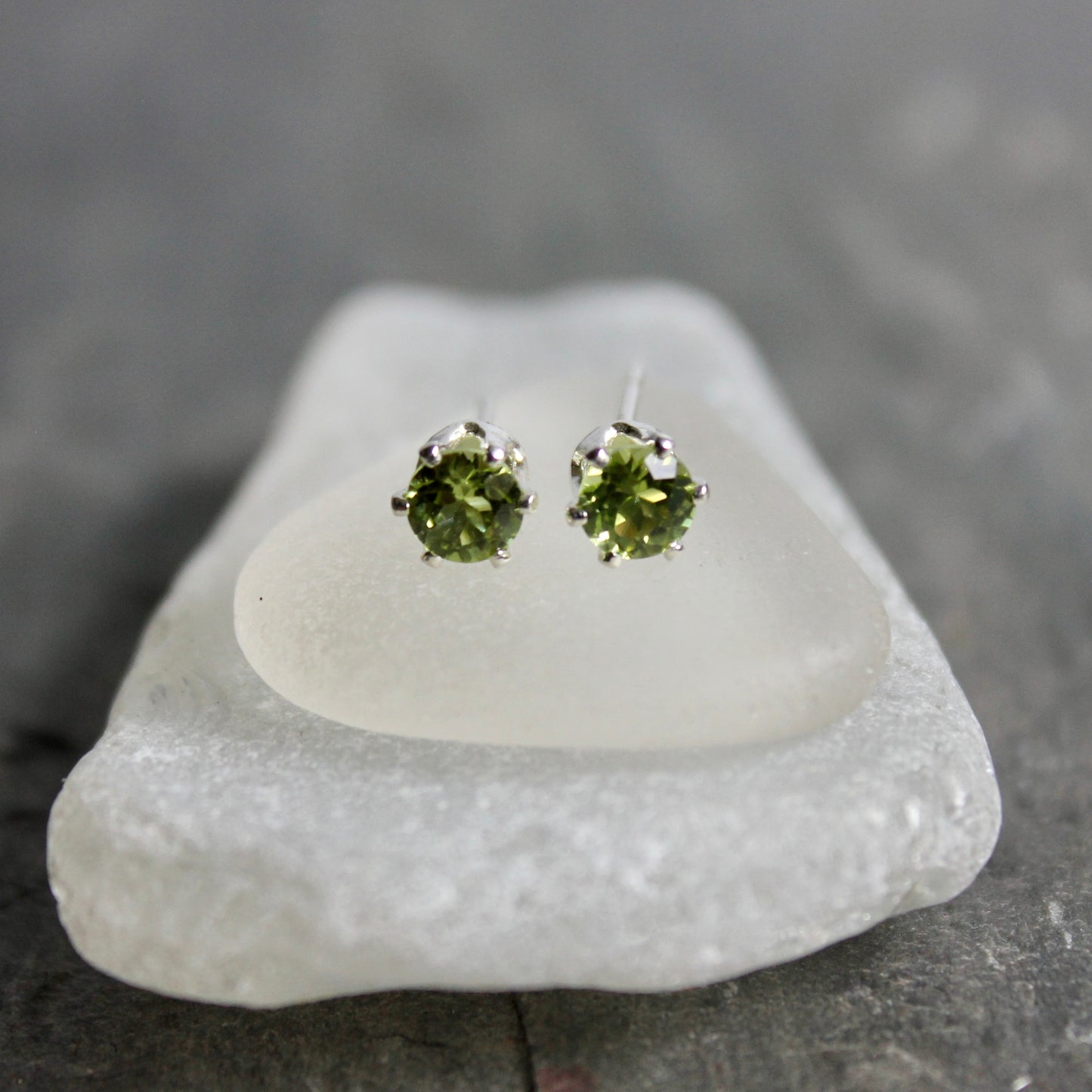 Green gemstone stud earrings on a white stone with a gray background
