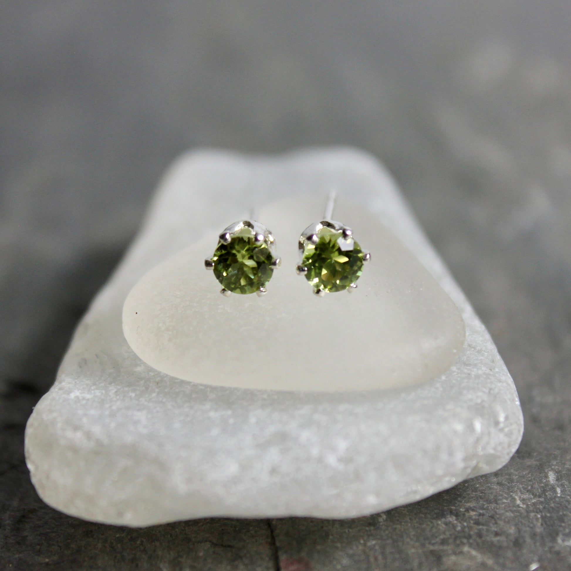 Green gemstone stud earrings on a white stone with a gray background