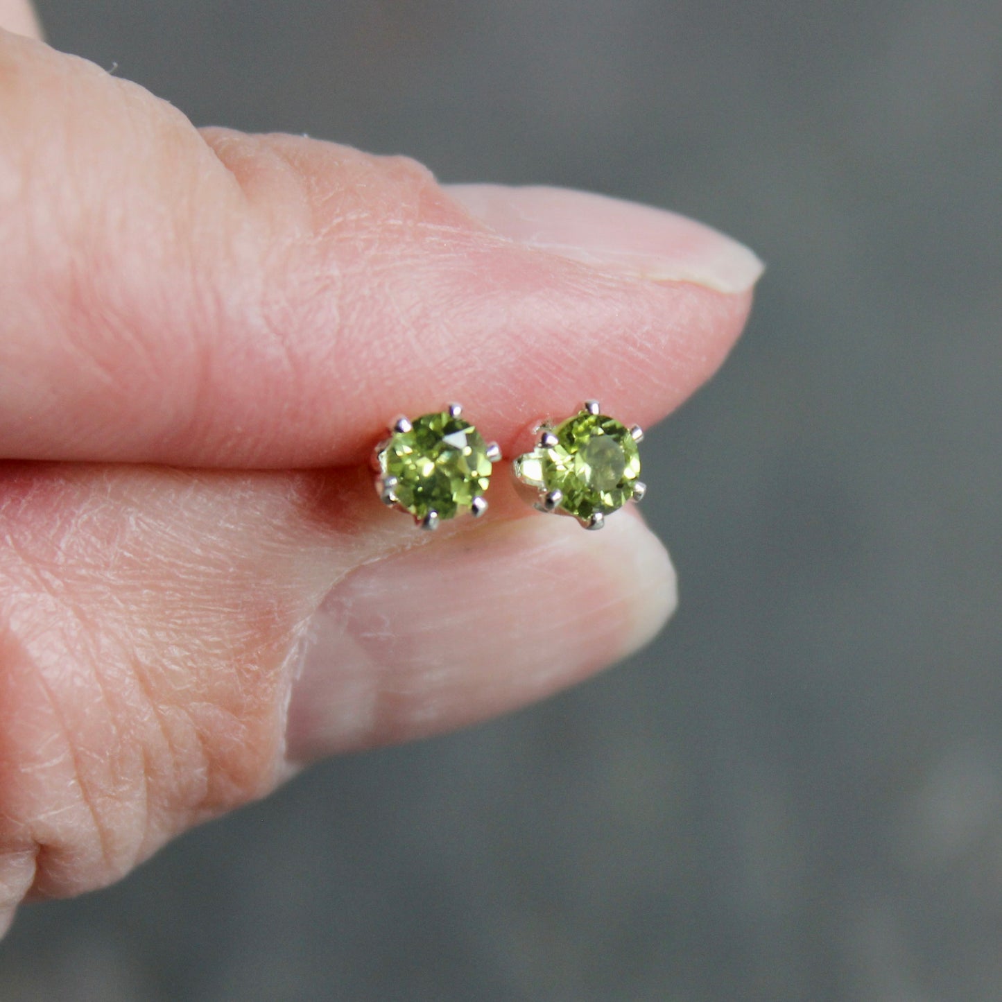 Peridot stud earrings held between fingers against a blurred background