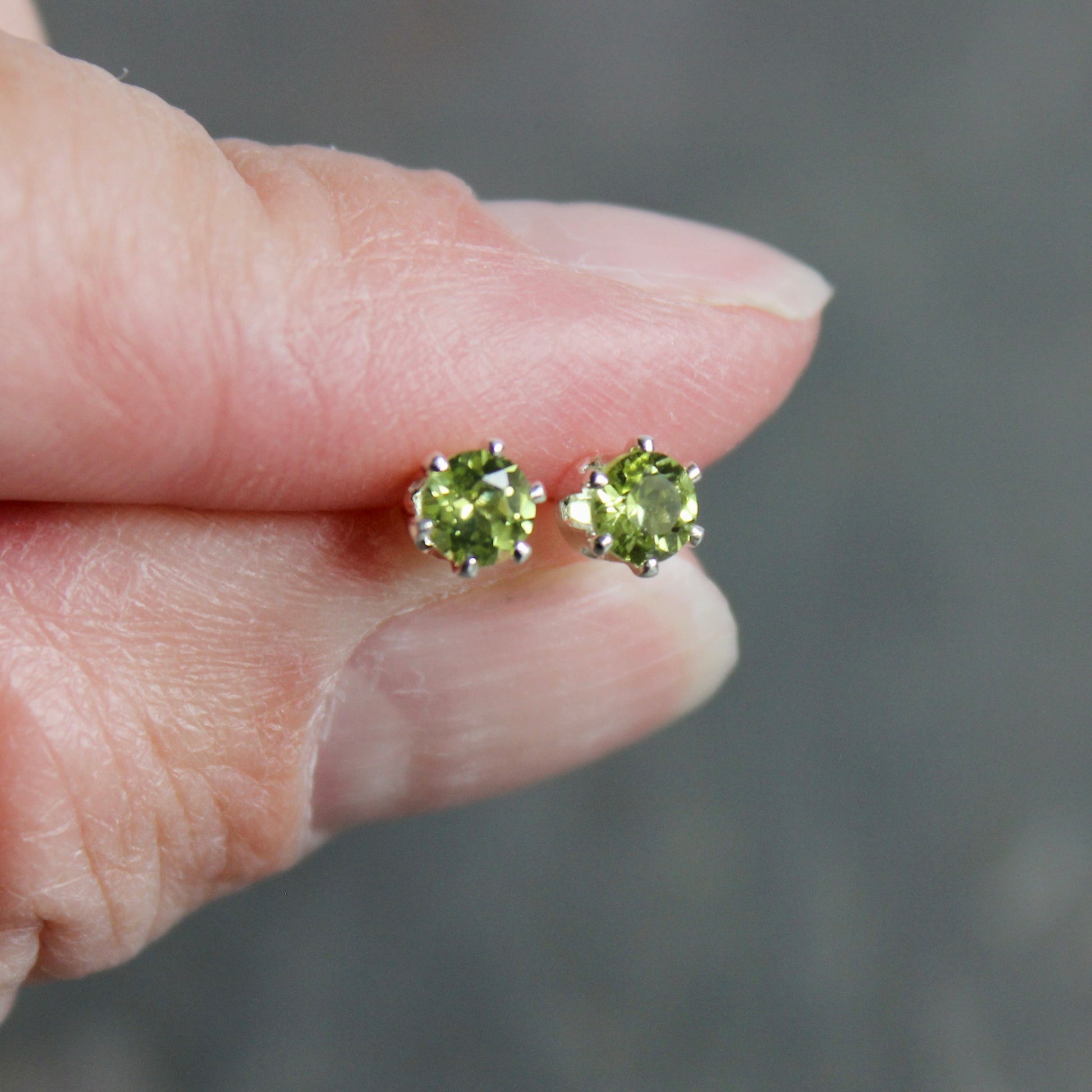 Peridot stud earrings held between fingers against a blurred background