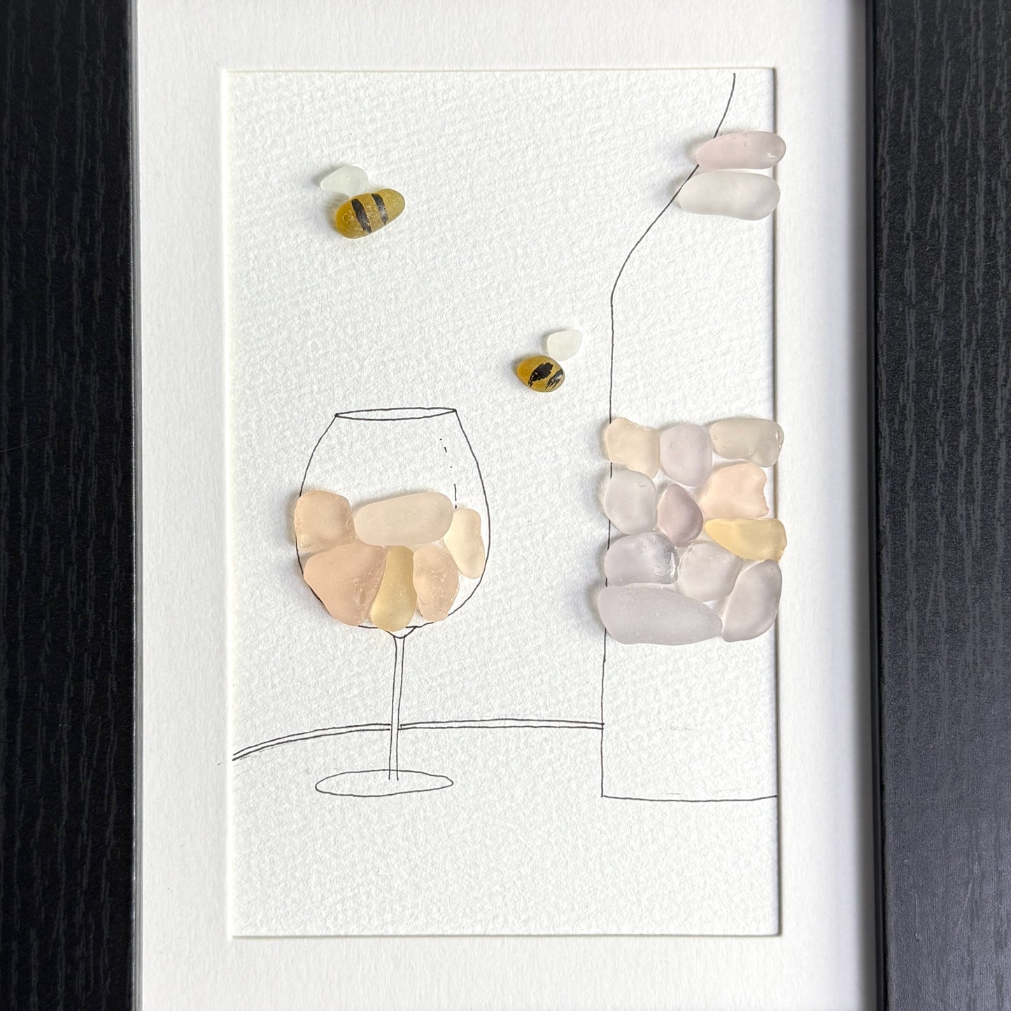 Decorative wall art with pebble art of a wine glass and bottle on a white background
