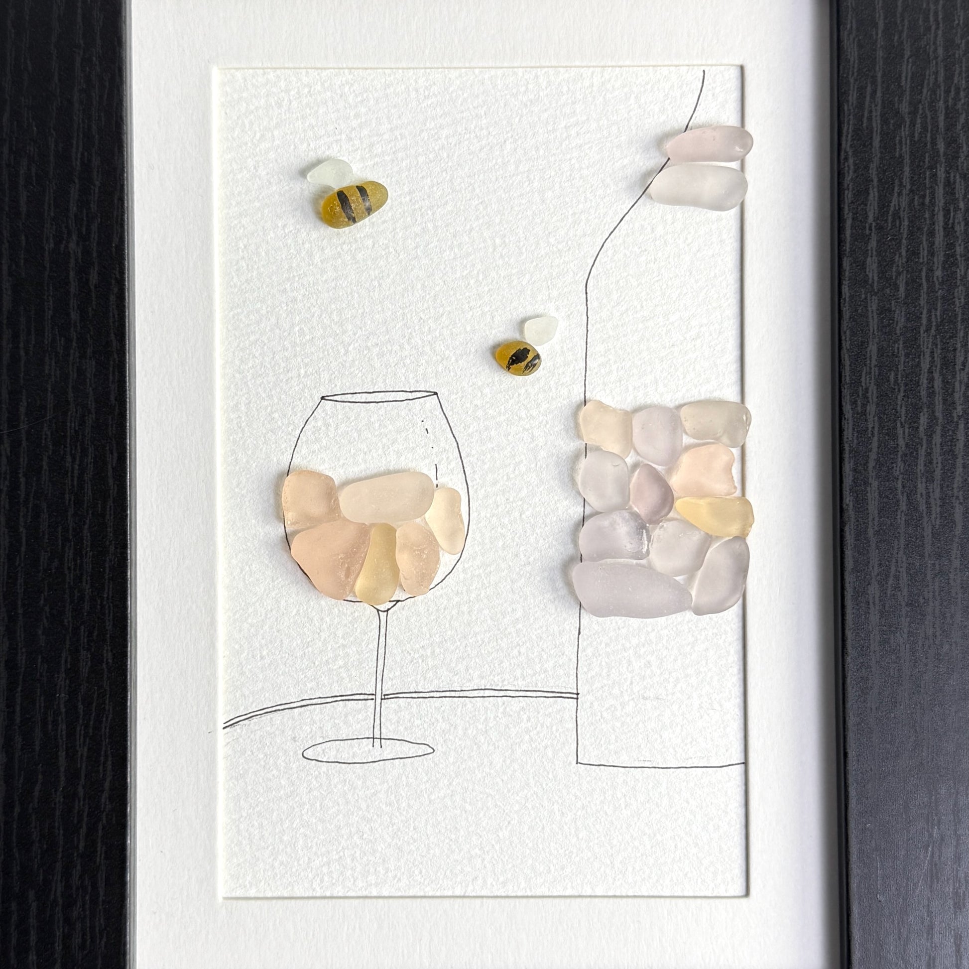 Decorative wall art with pebble art of a wine glass and bottle on a white background