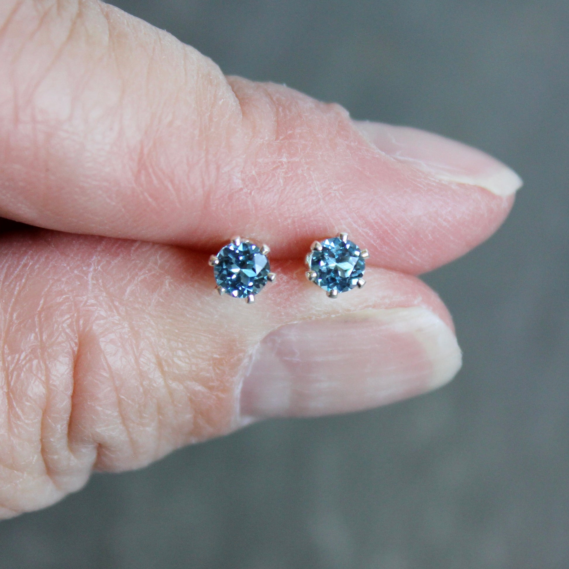 Blue gemstone earrings held between fingers against a neutral background