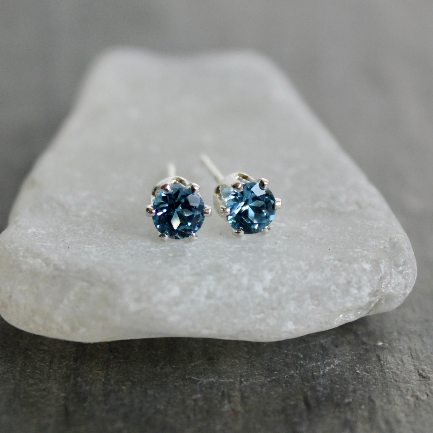 Pair of blue gemstone stud earrings on a gray stone surface