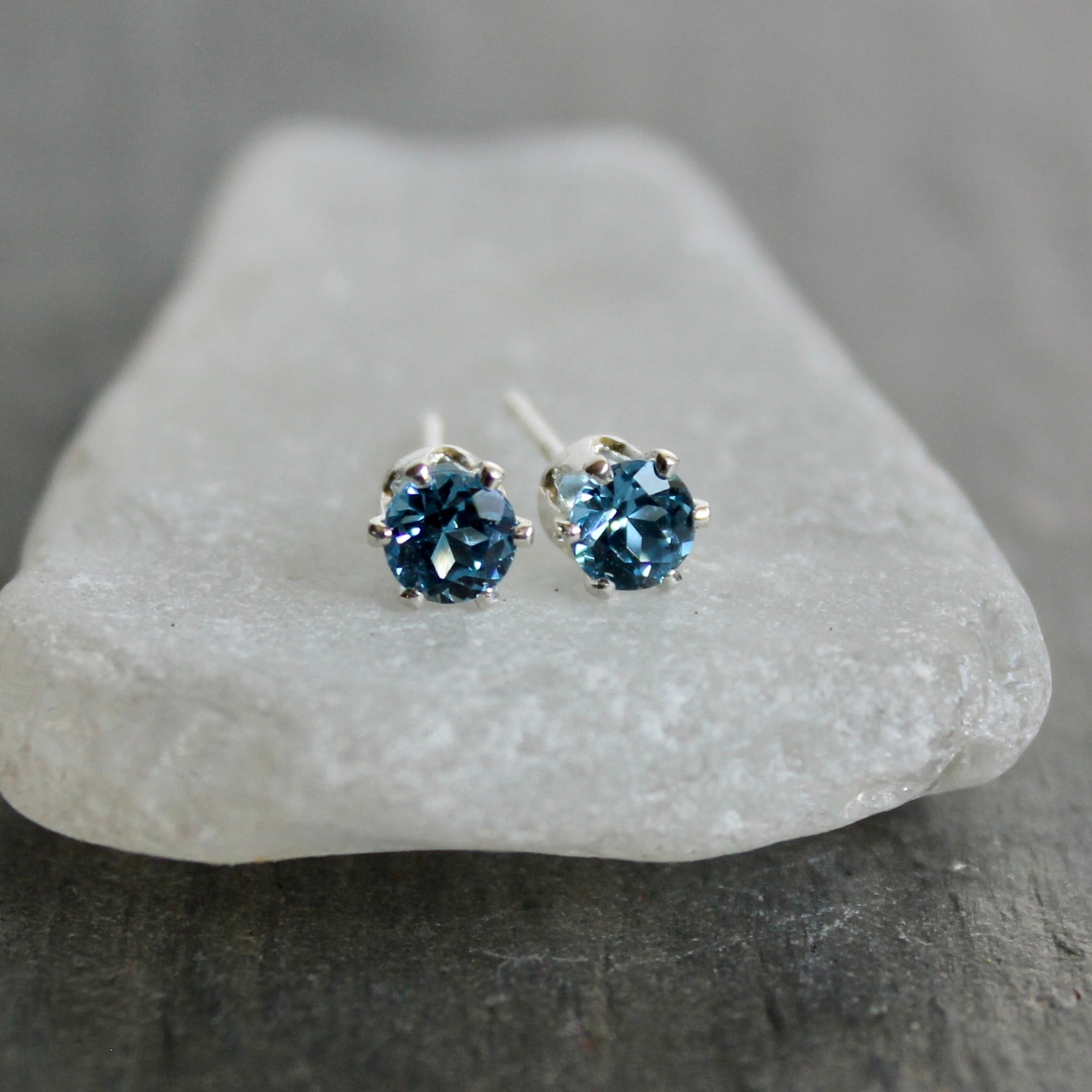 Pair of blue gemstone stud earrings on a gray stone surface