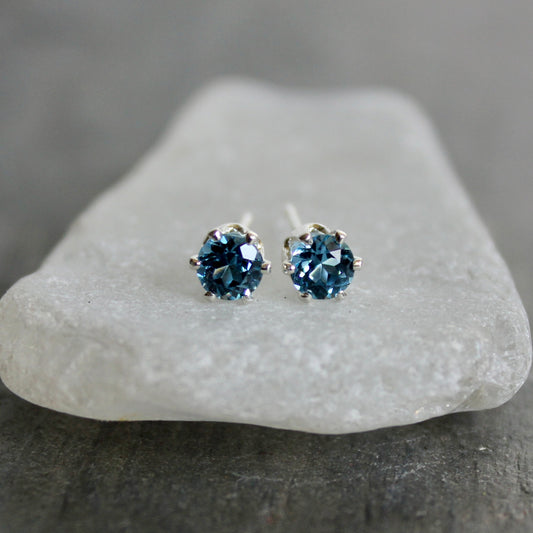 Pair of blue gemstone stud earrings on a white stone with a gray background