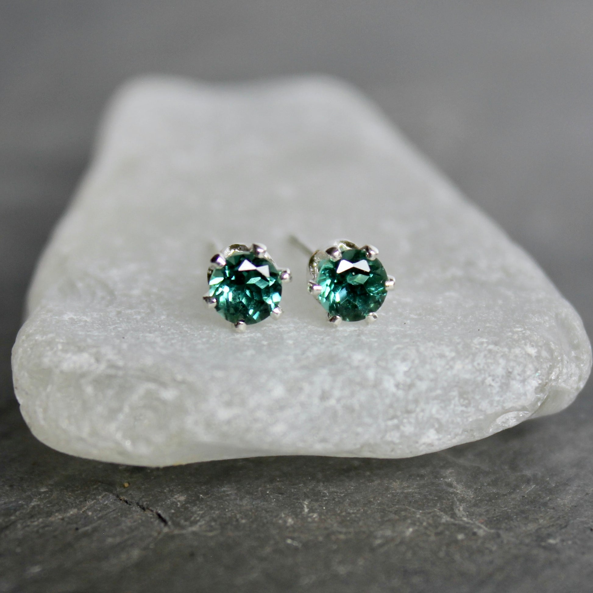 Green gemstone stud earrings on a white stone with a gray background