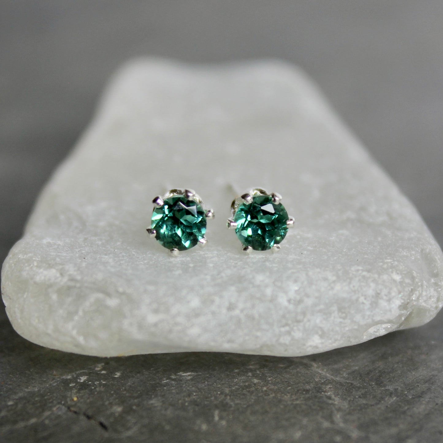Green gemstone stud earrings on a piece of white stone with a gray background