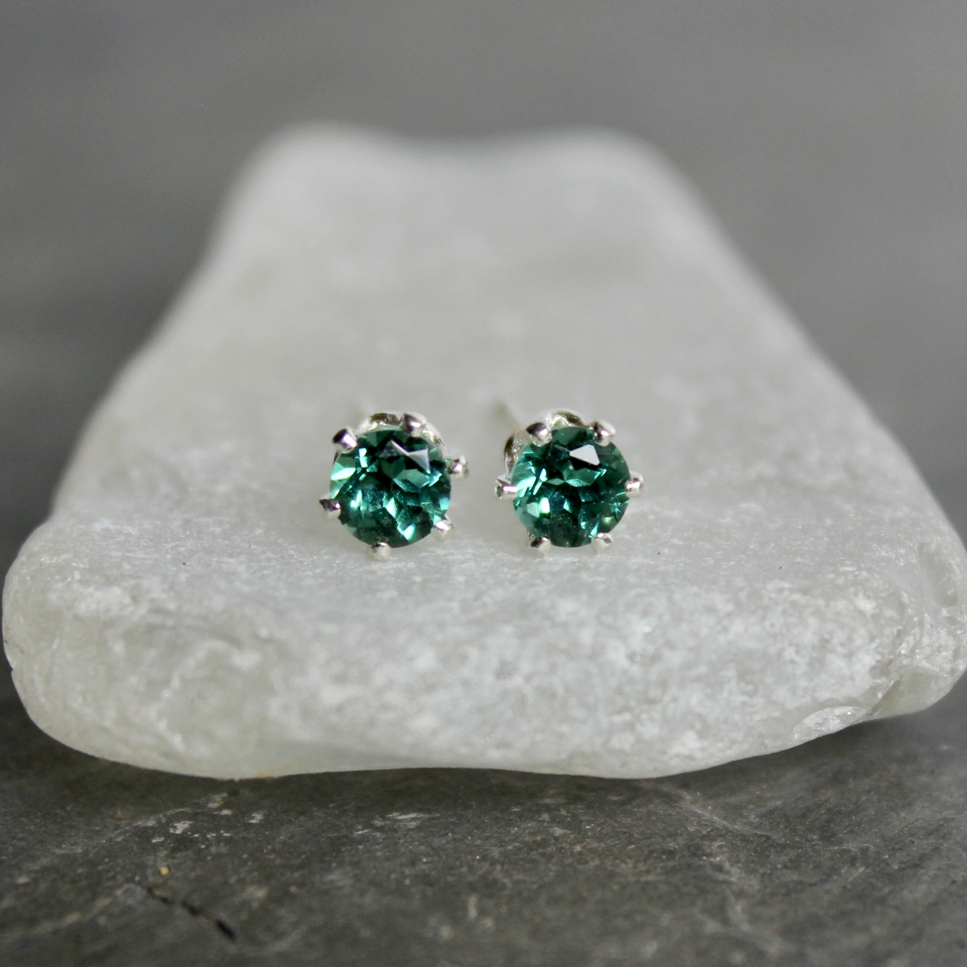Green gemstone stud earrings on a piece of white stone with a gray background