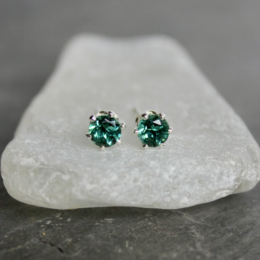 Green gemstone stud earrings on a piece of white stone with a gray background