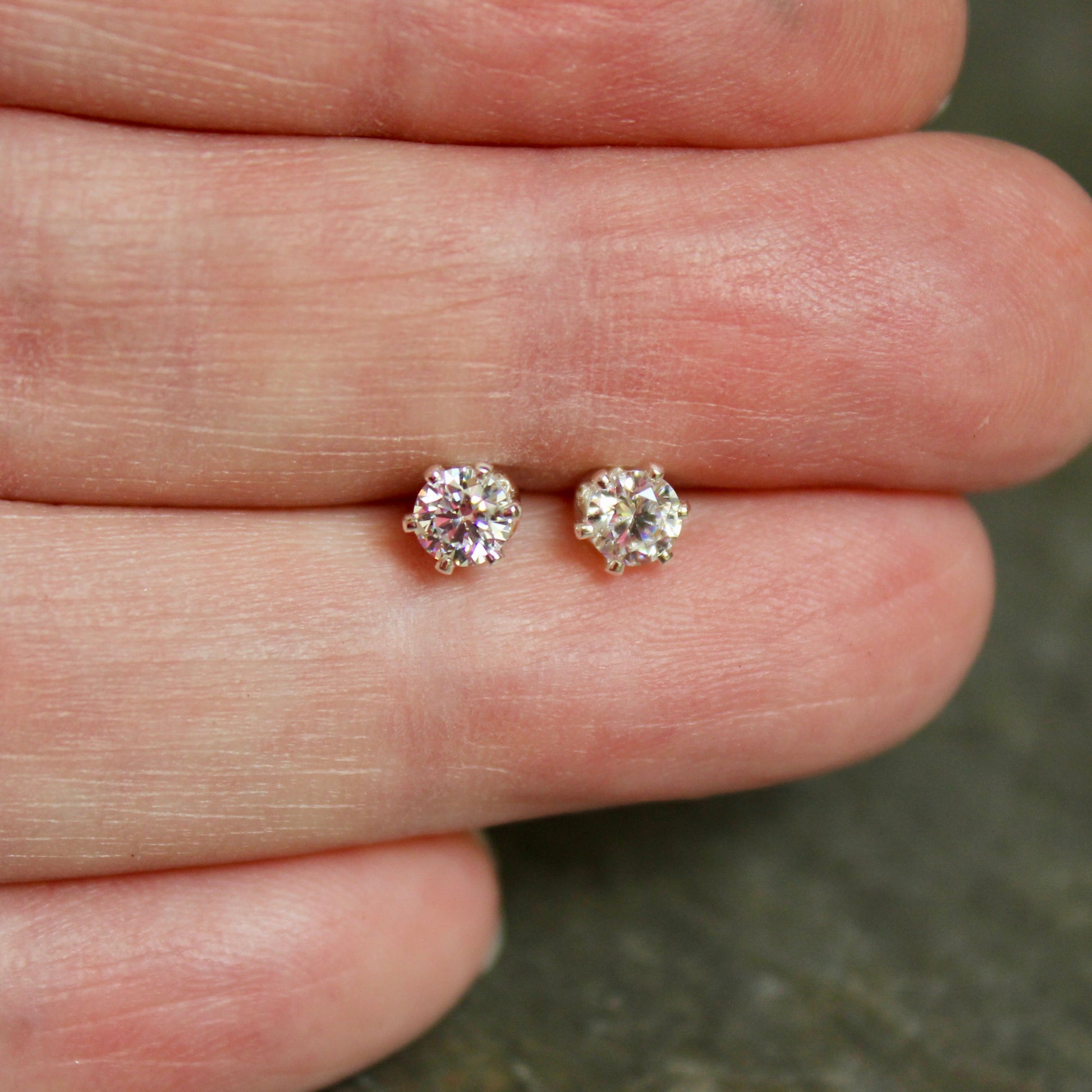 Two diamond stud earrings held between two fingers against a neutral background