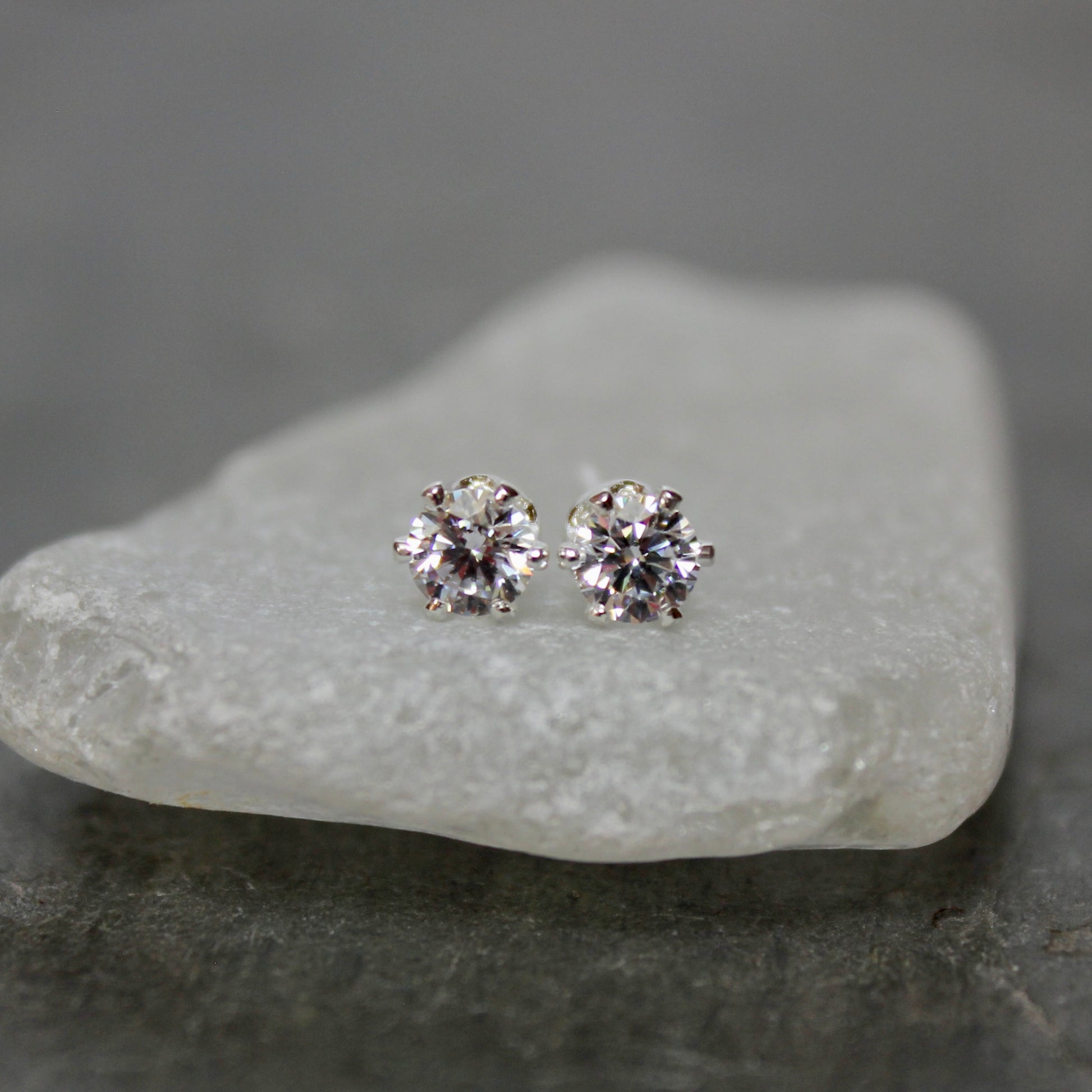 Diamond stud earrings on a piece of white stone with a gray background