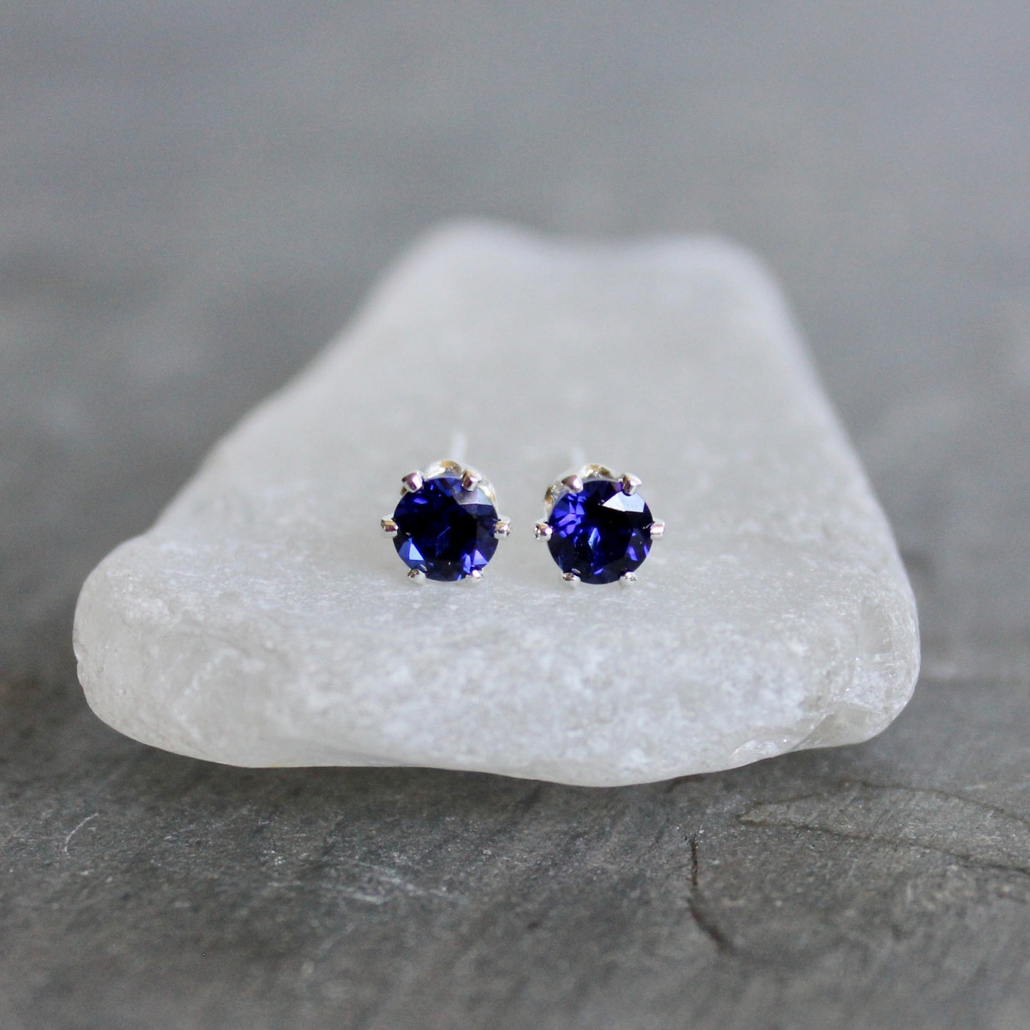 Pair of purple gemstone stud earrings on a white stone with a gray background