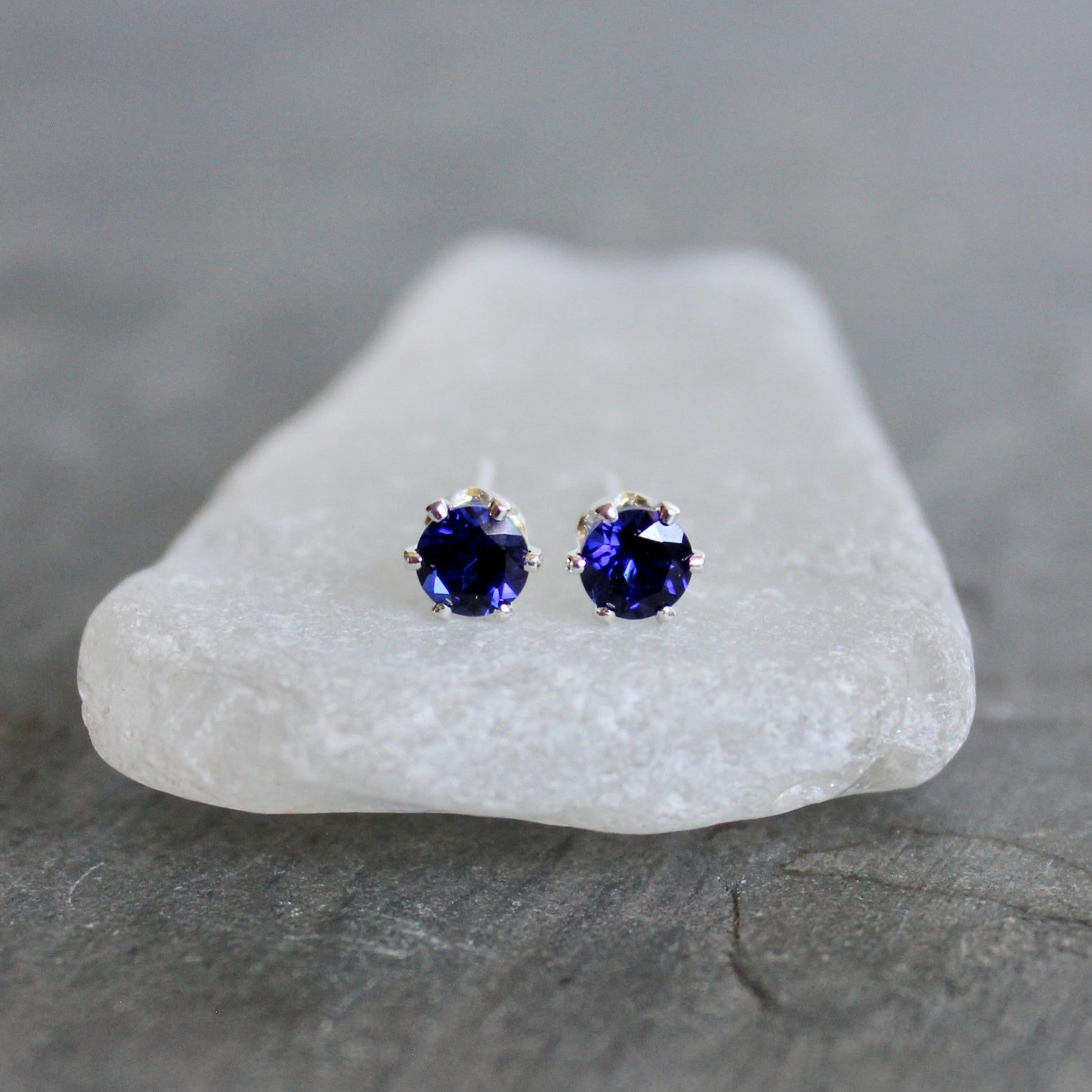 Pair of purple gemstone stud earrings on a white stone with a gray background