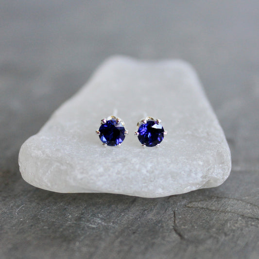 Pair of purple gemstone stud earrings on a white stone with a gray background