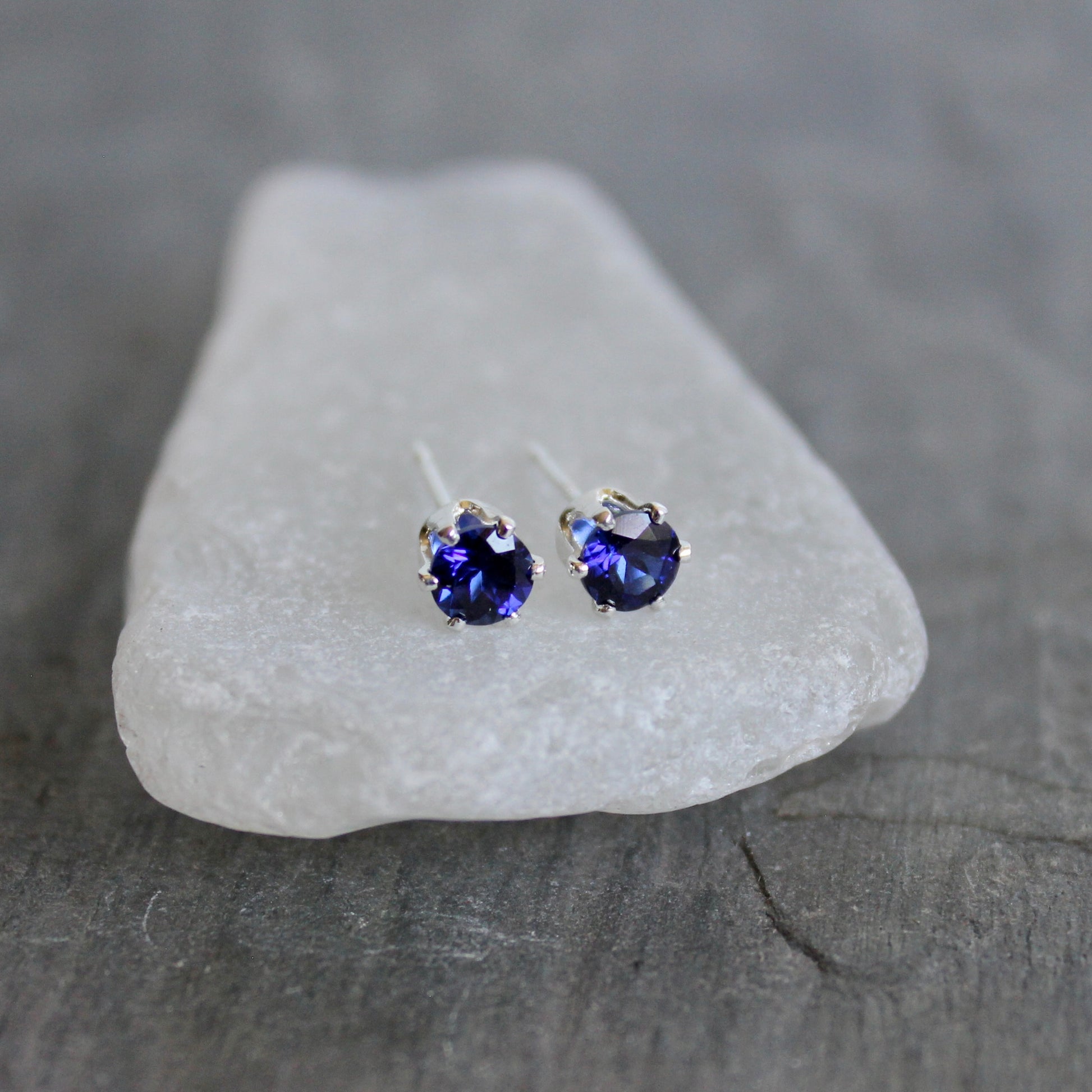 Pair of purple gemstone stud earrings on a white stone with a gray background