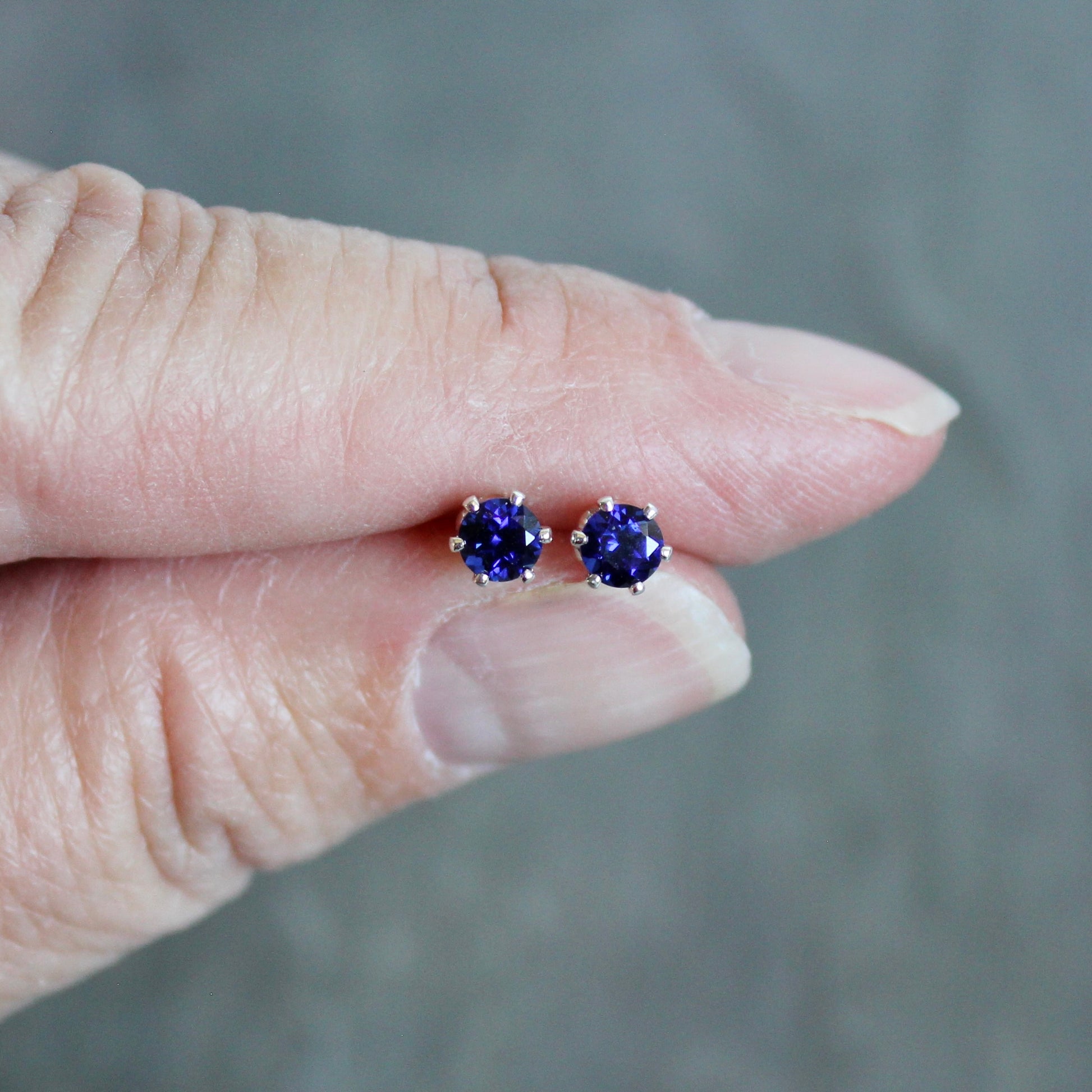Purple gemstone stud earrings held between fingers against a neutral background