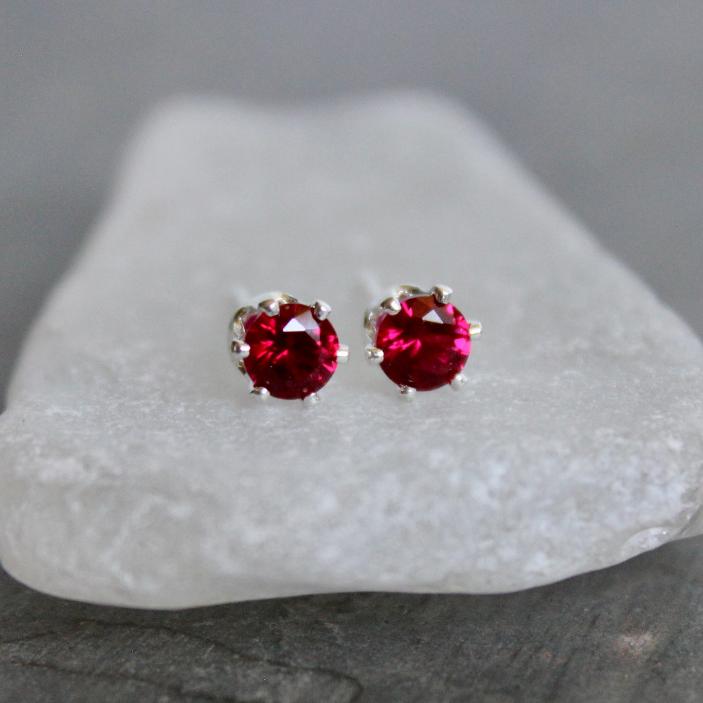 Red gemstone stud earrings on a white stand with a gray background