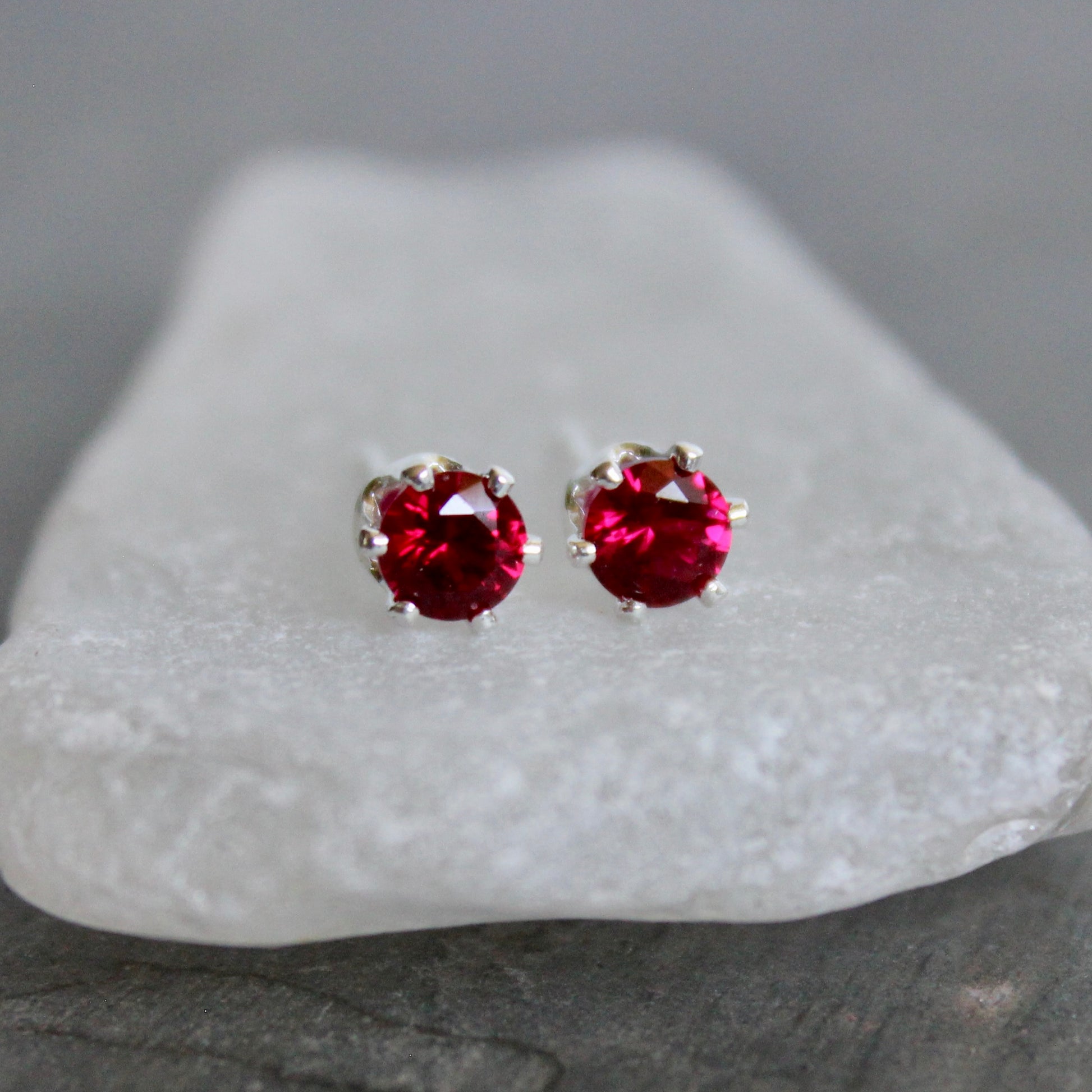 Red gemstone stud earrings on a white stand with a gray background