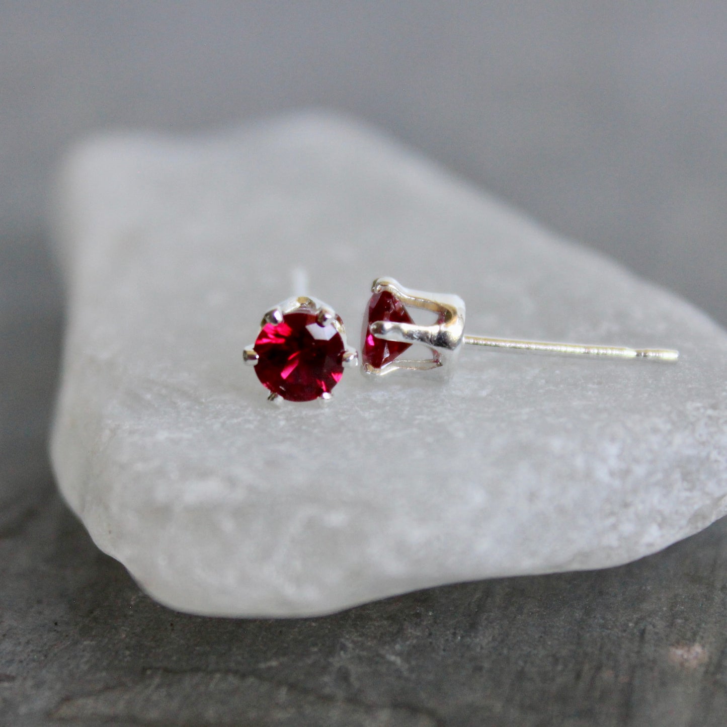 Pair of red gemstone stud earrings on a textured white stone