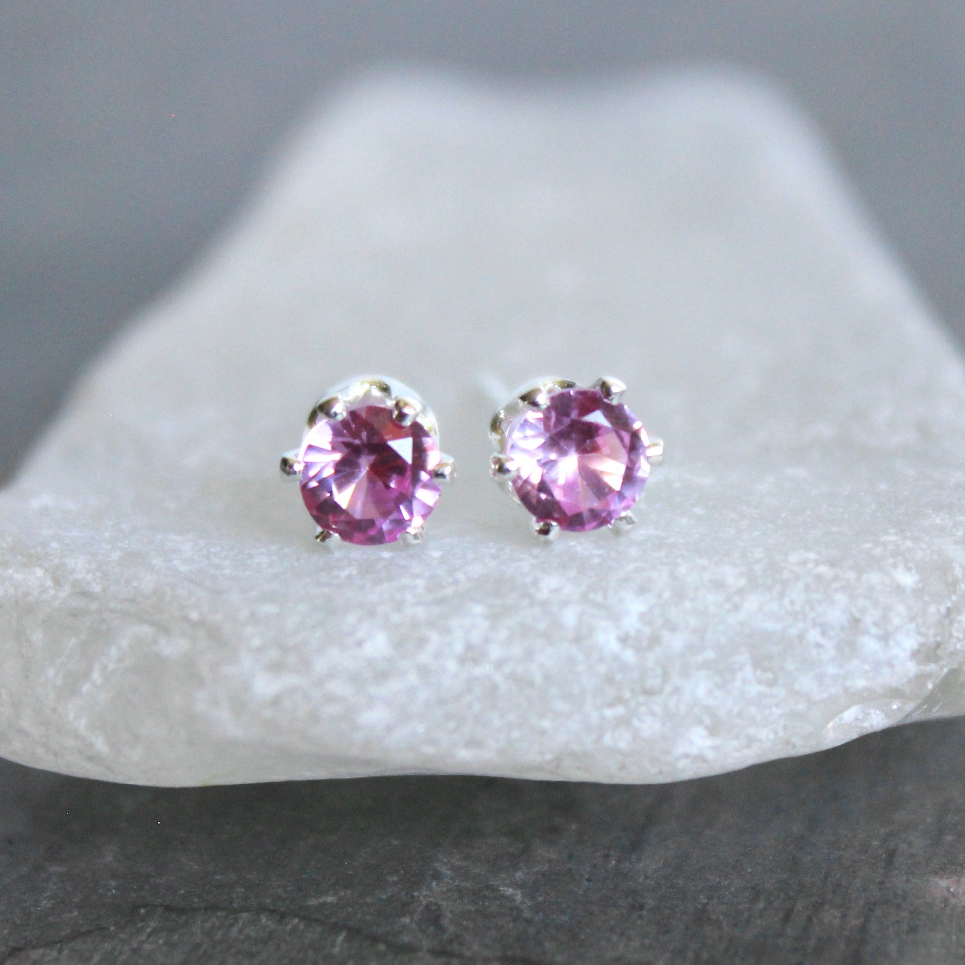 Purple gemstone stud earrings on a white stone with a gray background