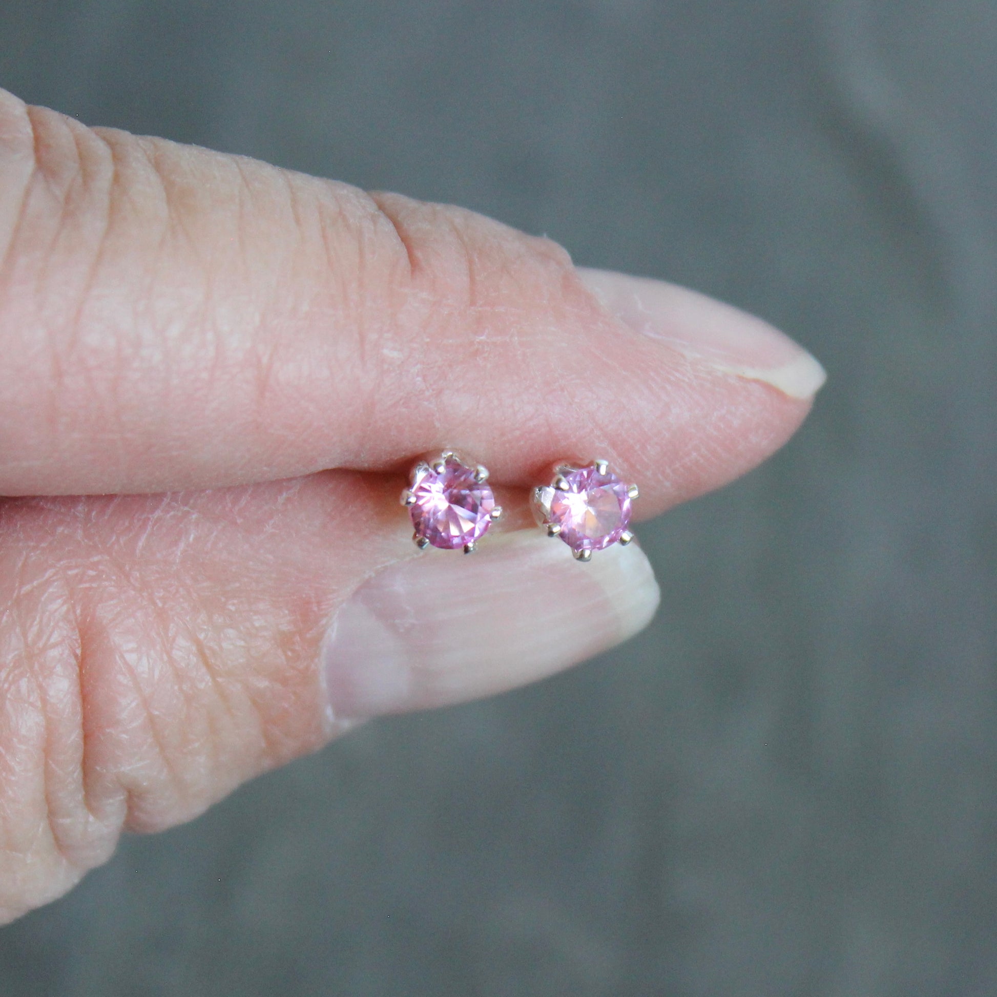 Pink gemstone stud earrings held between fingers against a neutral background
