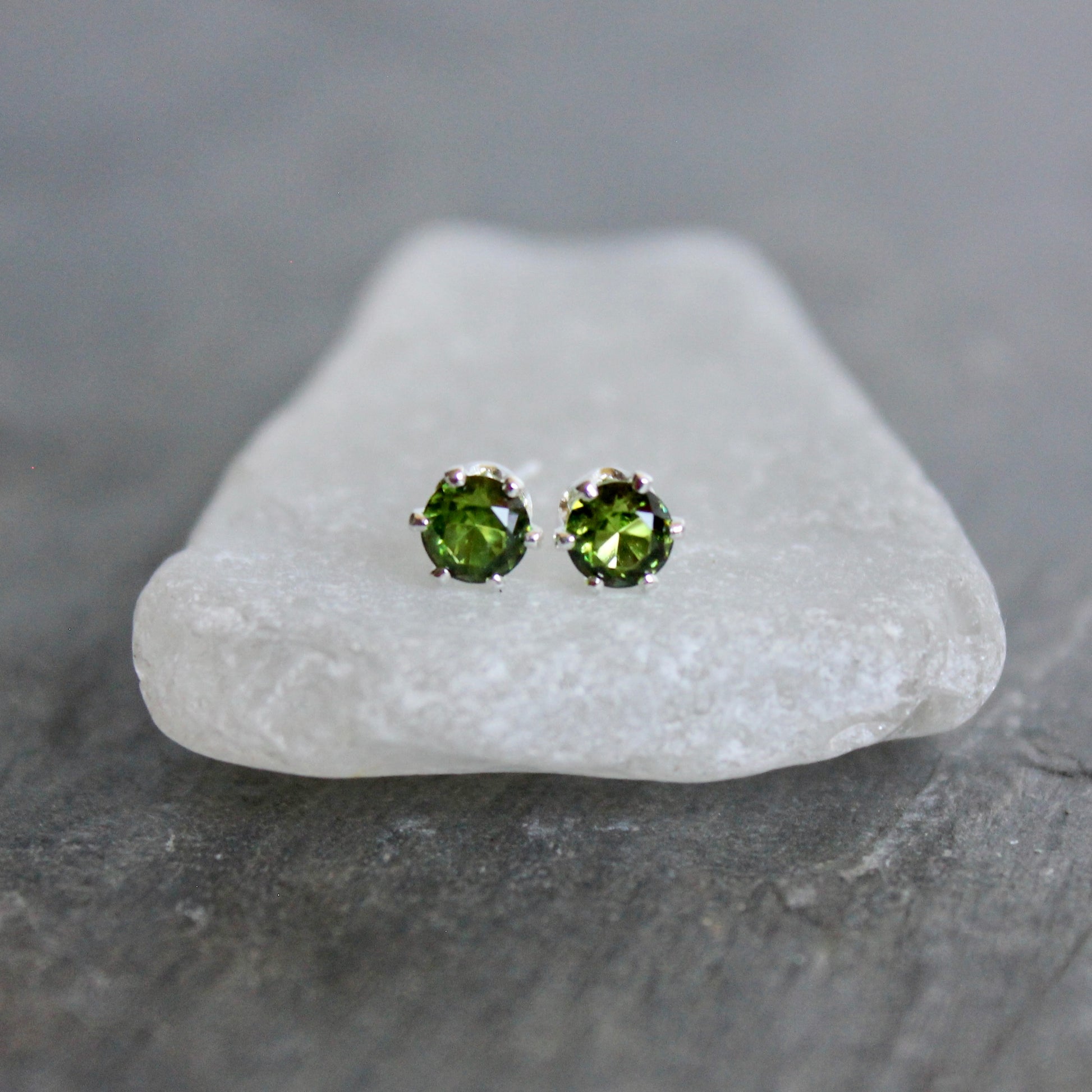 Green gemstone stud earrings on a white stone with a gray background