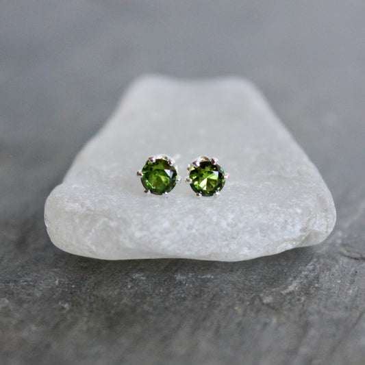 Green gemstone stud earrings on a white stone with a gray background