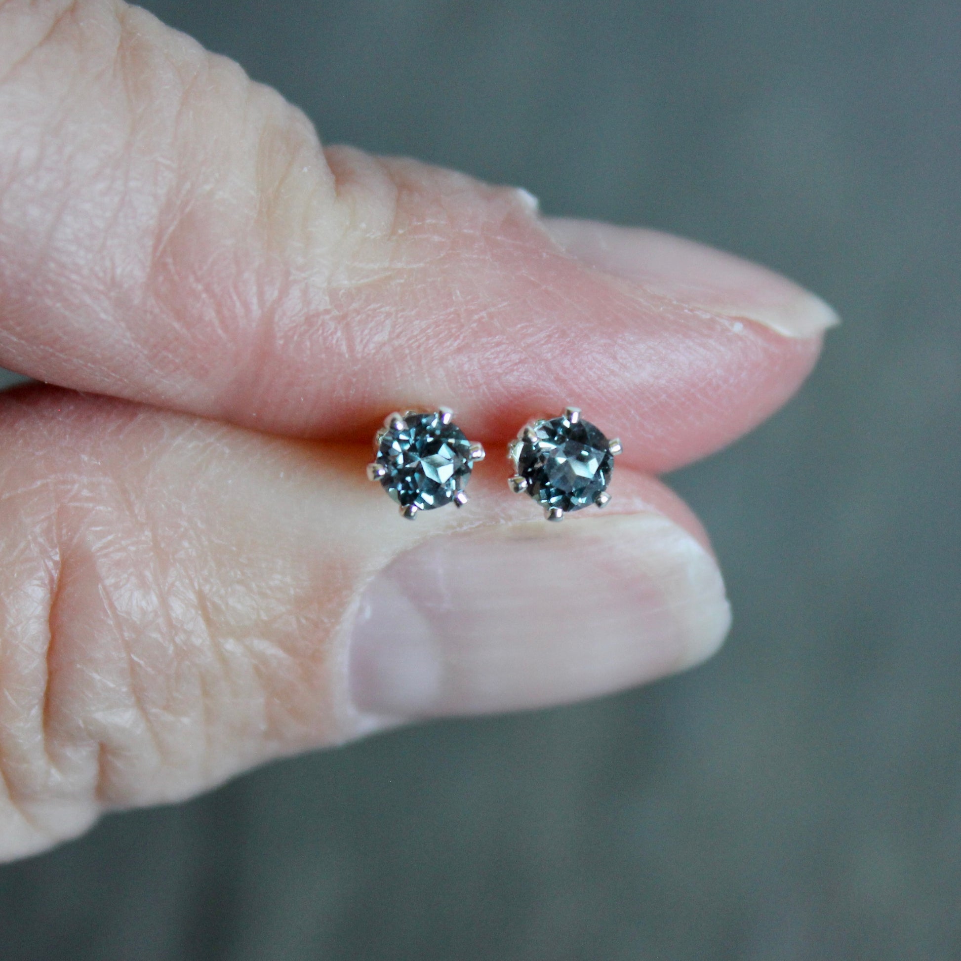 Pair of diamond stud earrings held between two fingers against a neutral background