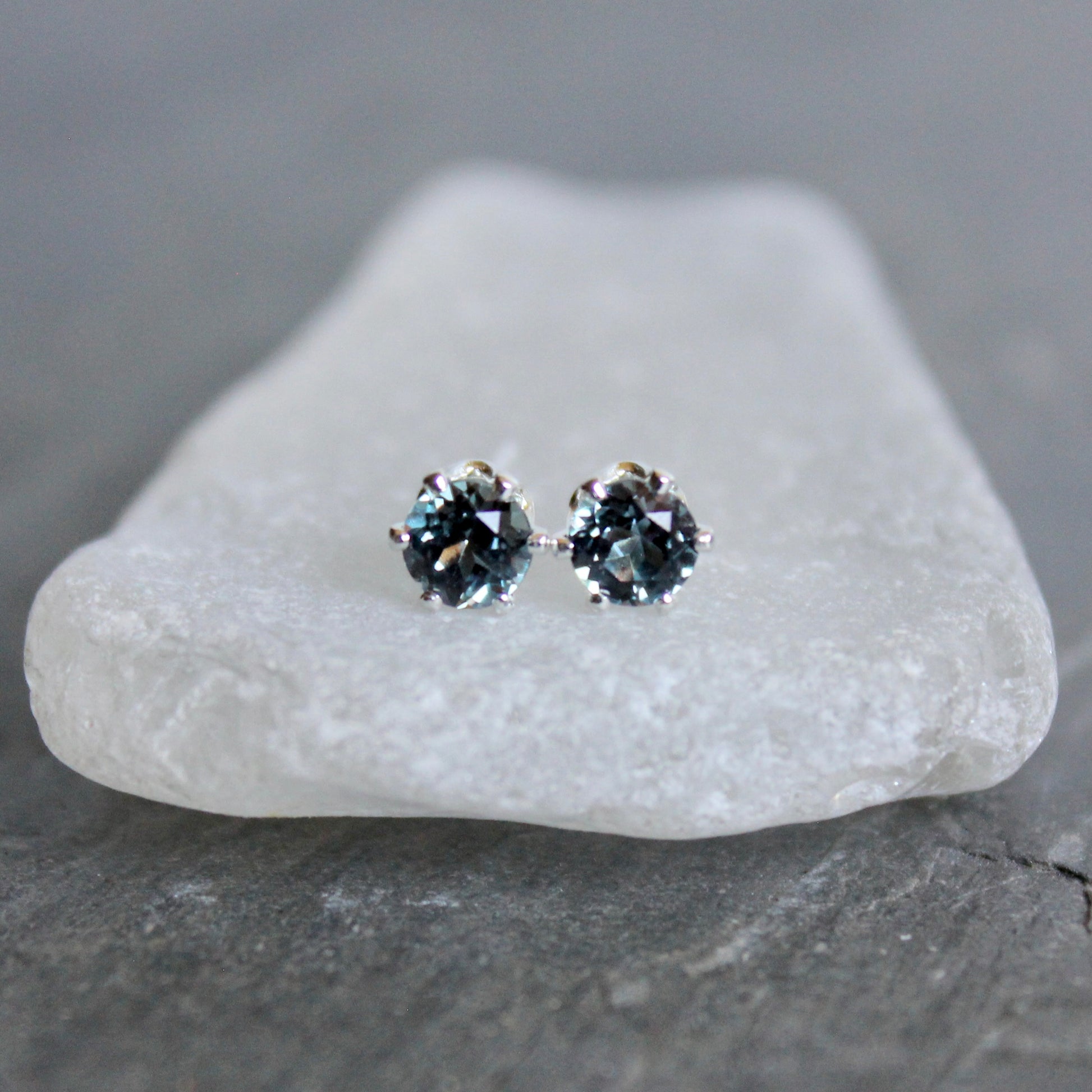 Pair of silver stud earrings with blue gemstones on a white stone.