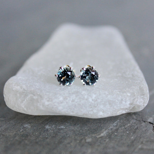 Pair of silver stud earrings with blue gemstones on a white stone.