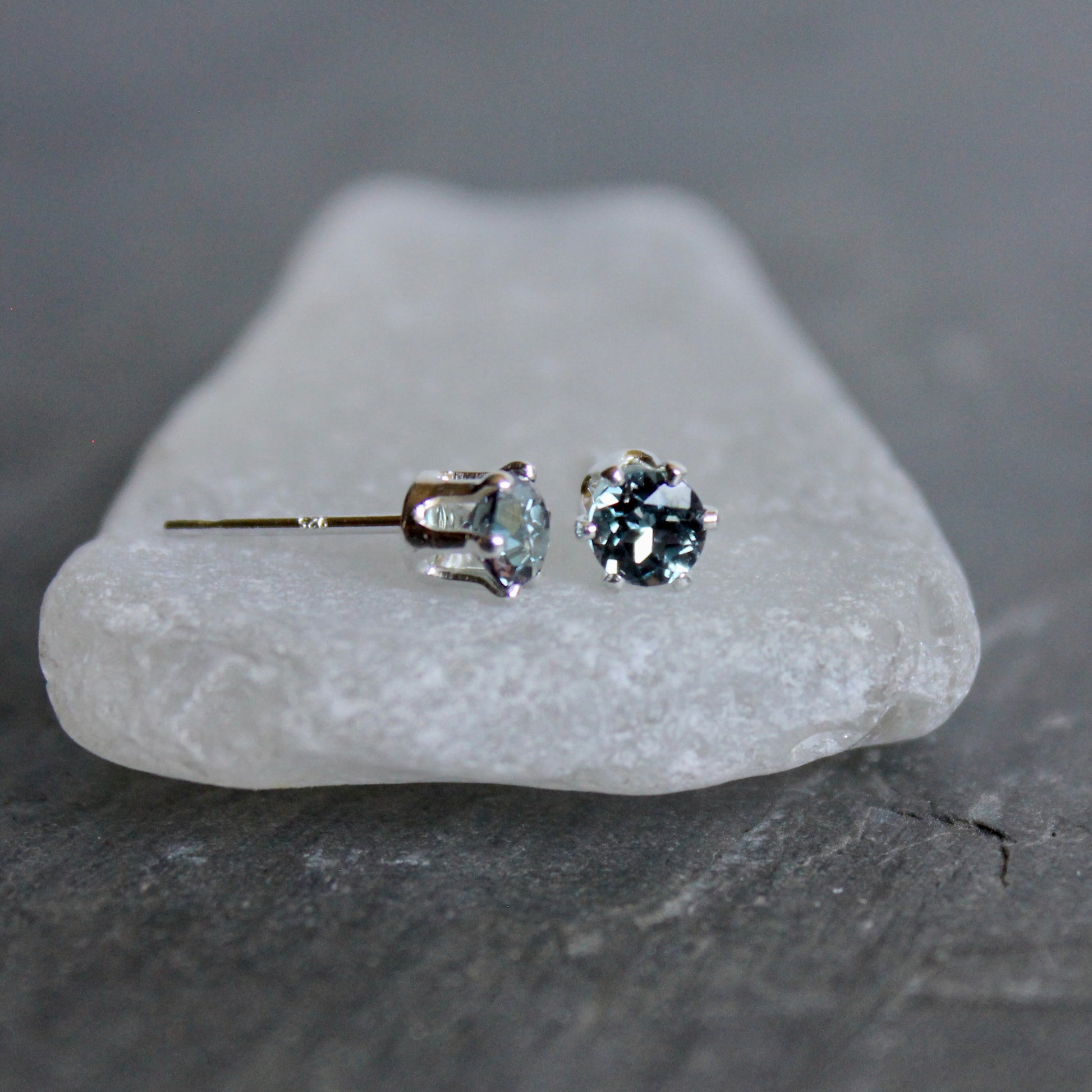Pair of gemstone stud earrings on a piece of white stone with a dark background