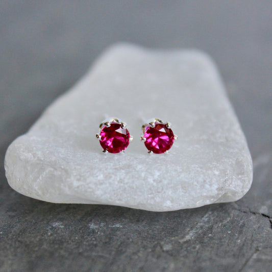 Pair of lab created ruby gemstone stud earrings on a white stone with a gray background
