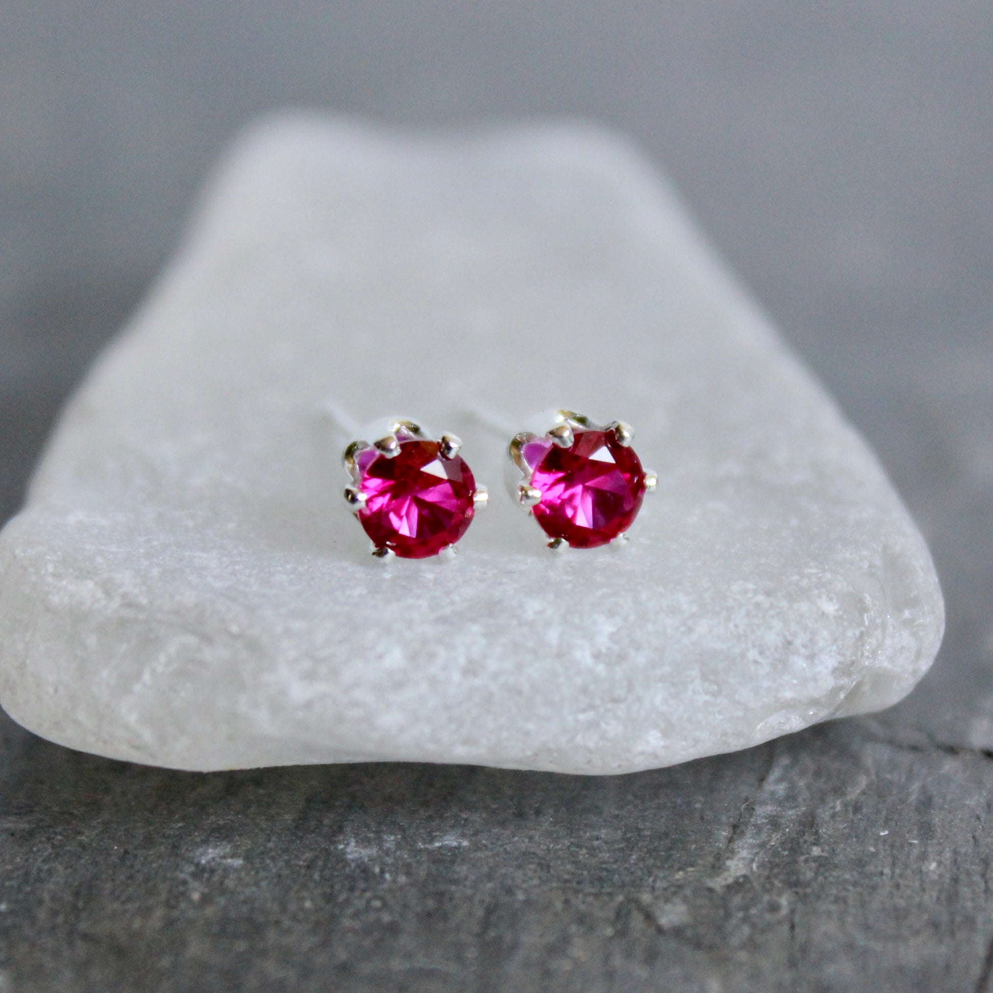 Pair of lab created ruby gemstone stud earrings on a white stone surface