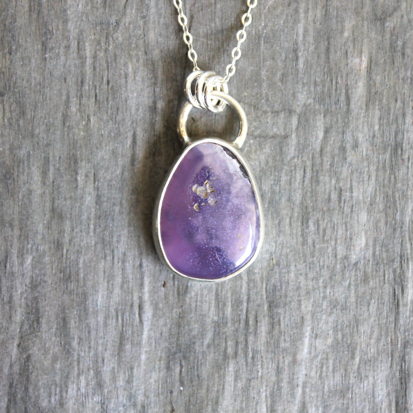Purple teardrop pendant on a silver chain against a wooden background. A holley blue agate cabochon set in a fine and sterling silver bezel setting on a sturdy silver chain. 