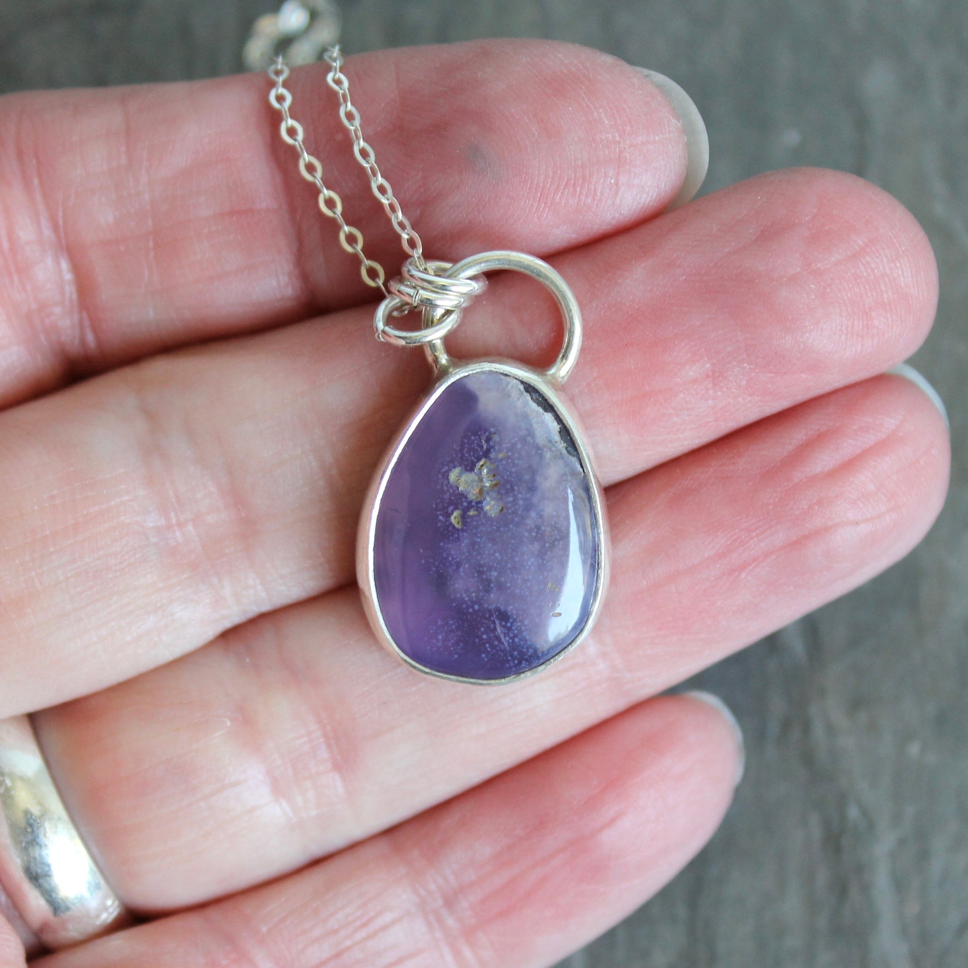 Indigo pendant on a silver chain held in a hand against a neutral. A holley blue agate cabochon set in a fine and sterling silver bezel setting on a sturdy silver chain.  background