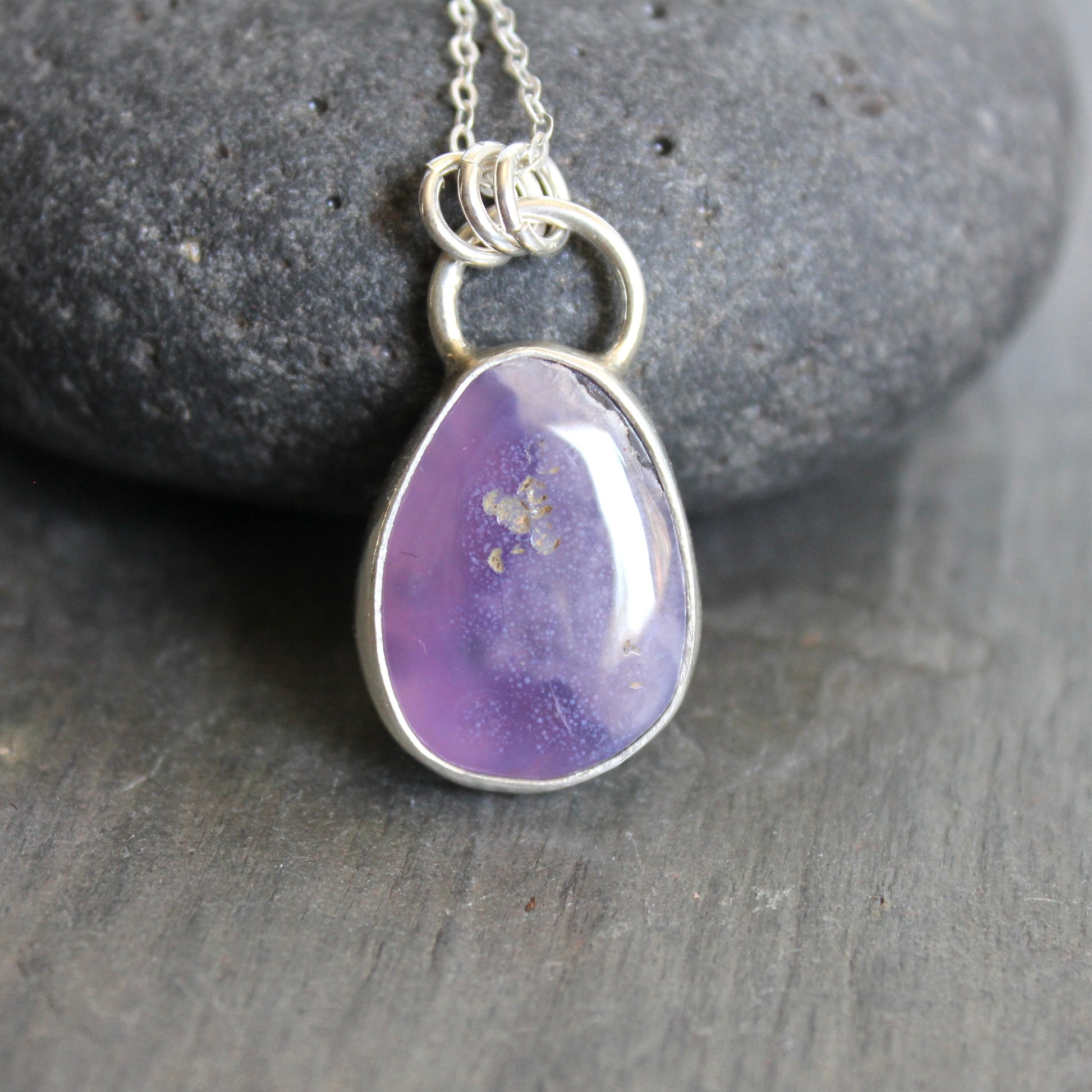 Purple teardrop pendant on a silver chain against a gray stone background. A holley blue agate cabochon set in a fine and sterling silver bezel setting on a sturdy silver chain.  