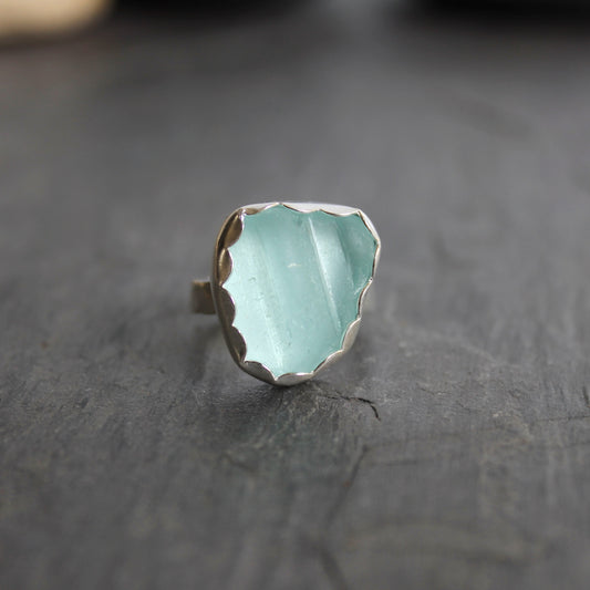 This statement ring has a pale aqua blue piece of sea glass that is set in a fine and sterling silver scalloped bezel on a sturdy hammered band. This piece is actually from a bottle neck. Handmade by Barb Macy in Corvallis, OR. Size 5 