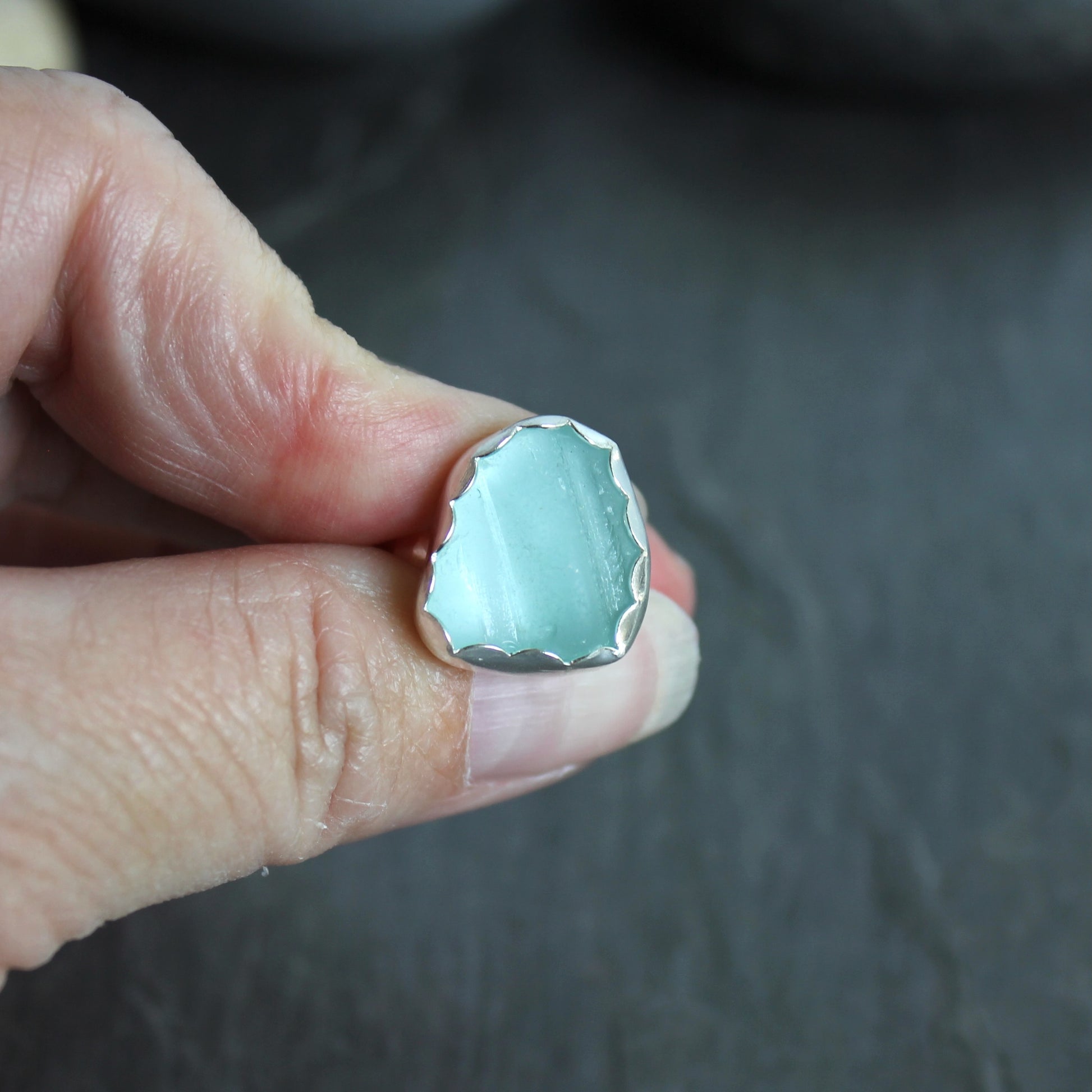 This statement ring has a pale aqua blue piece of sea glass that is set in a fine and sterling silver scalloped bezel on a sturdy hammered band. This piece is actually from a bottle neck. Handmade by Barb Macy in Corvallis, OR. Size 5 