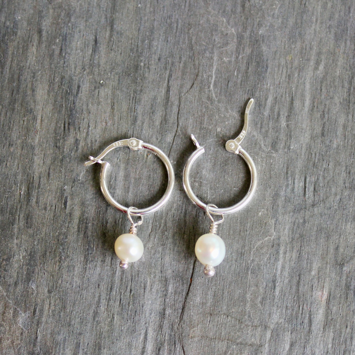 Silver hoop earrings with pearl drops on a gray stone surface. These locking hoops are approximately 15mm in diameter with a removeable freshwater pearl drop.