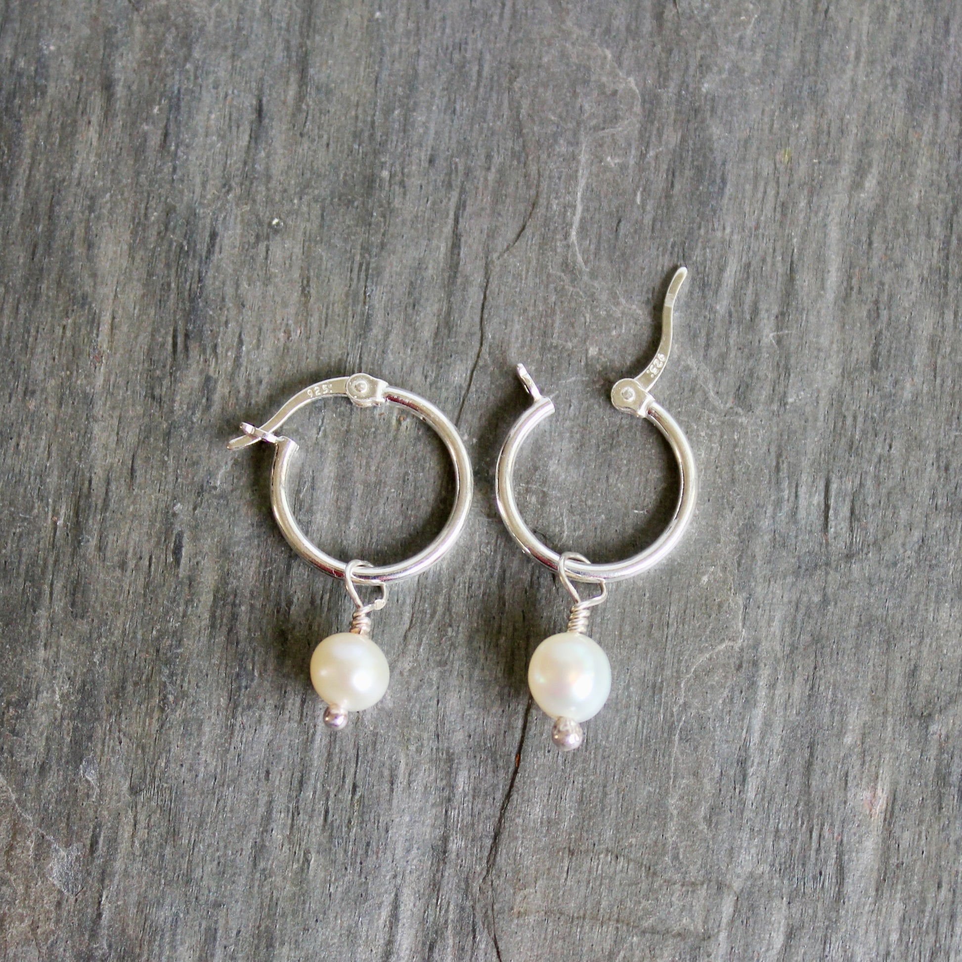 Silver hoop earrings with pearl drops on a gray stone surface. These locking hoops are approximately 15mm in diameter with a removeable freshwater pearl drop.