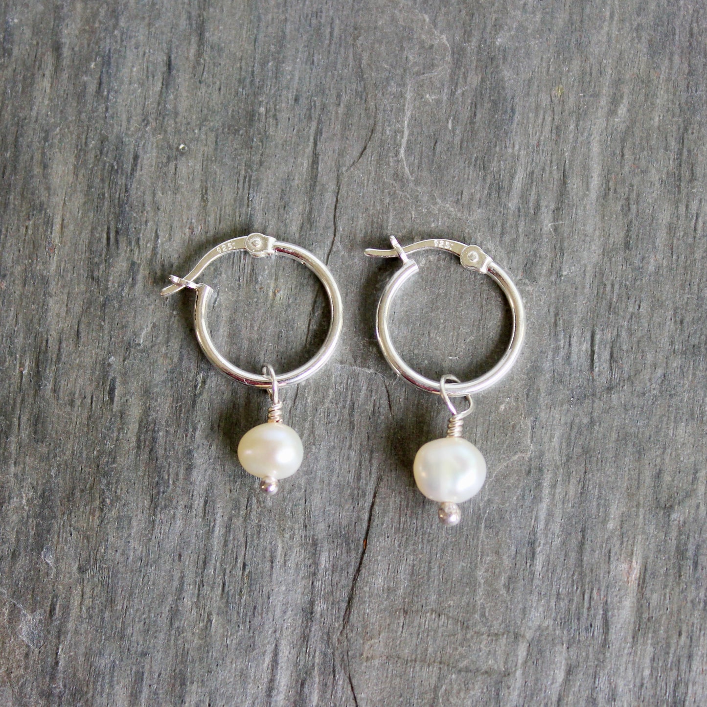 Silver hoop earrings with pearl drops on a gray wooden surface. These locking hoops are approximately 15mm in diameter with a removeable freshwater pearl drop.