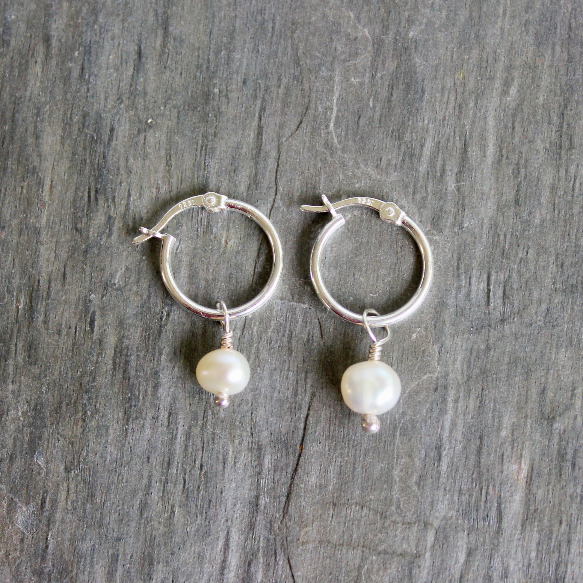 Silver hoop earrings with pearl drops on a gray wooden surface. These locking hoops are approximately 15mm in diameter with a removeable freshwater pearl drop.