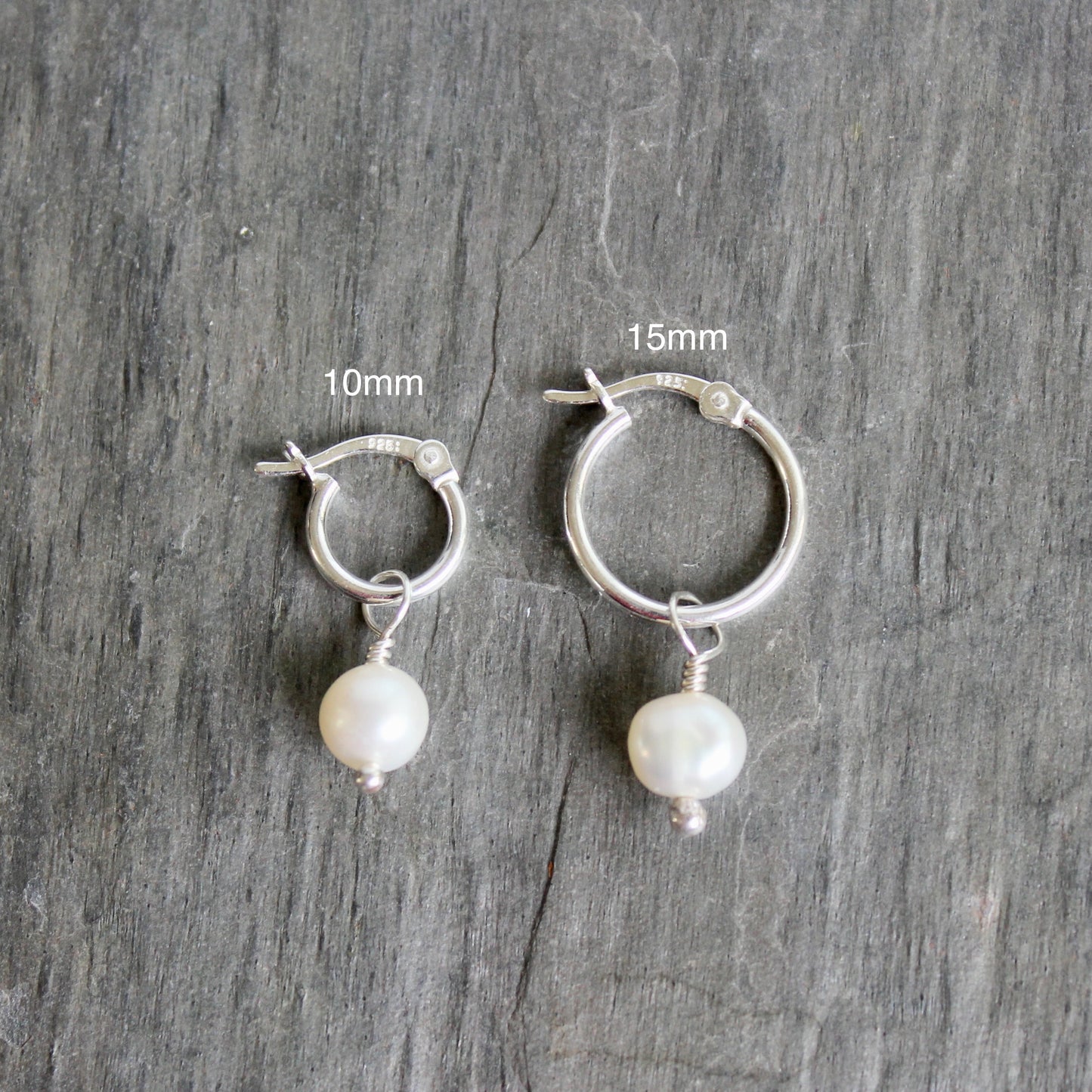 Silver hoop earrings with pearl drops on a gray wooden surface, showing size measurements. These locking hoops are approximately 10mm in diameter with a removable freshwater pearl drop.