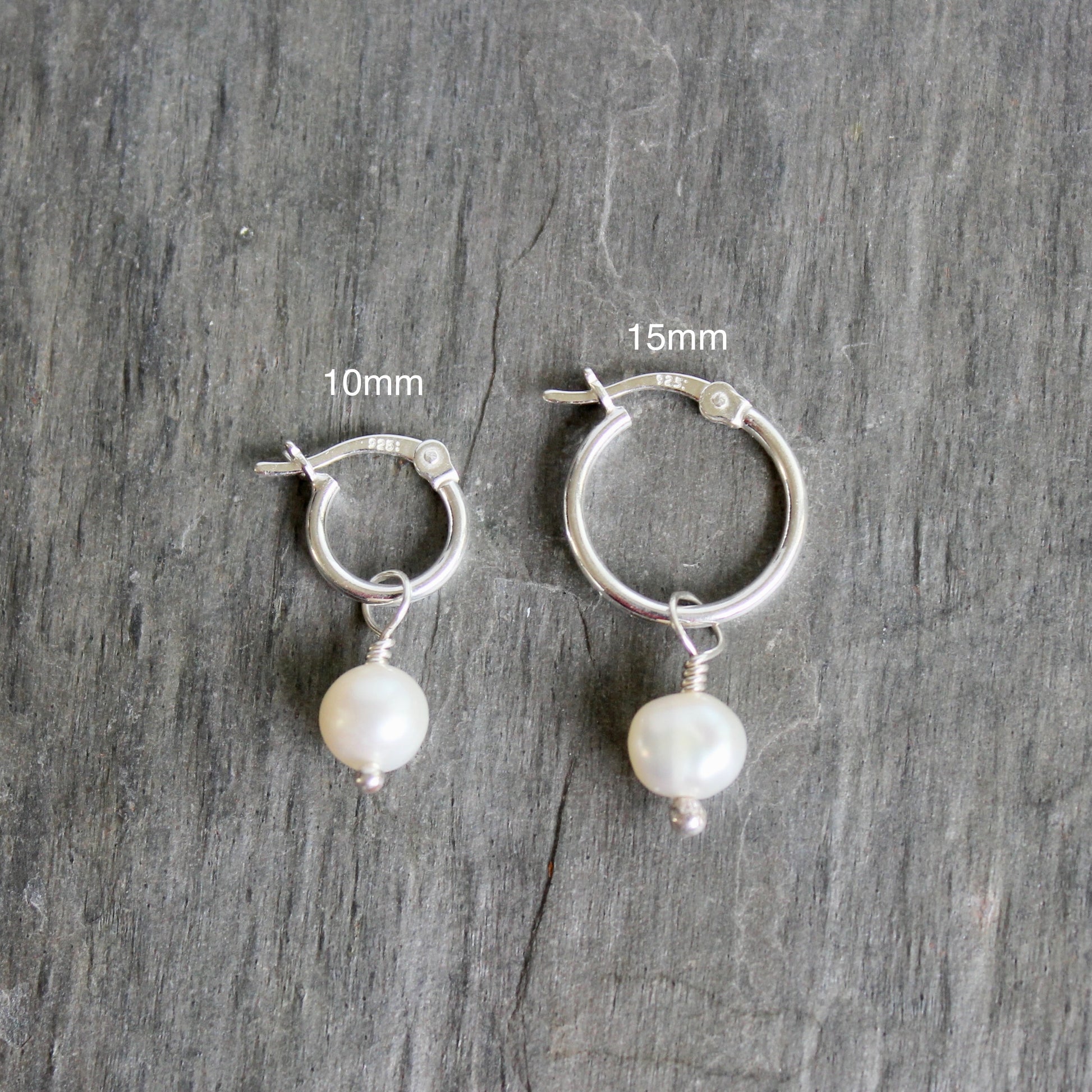 Silver hoop earrings with pearl drops on a gray wooden surface, showing size measurements. These locking hoops are approximately 10mm in diameter with a removable freshwater pearl drop.