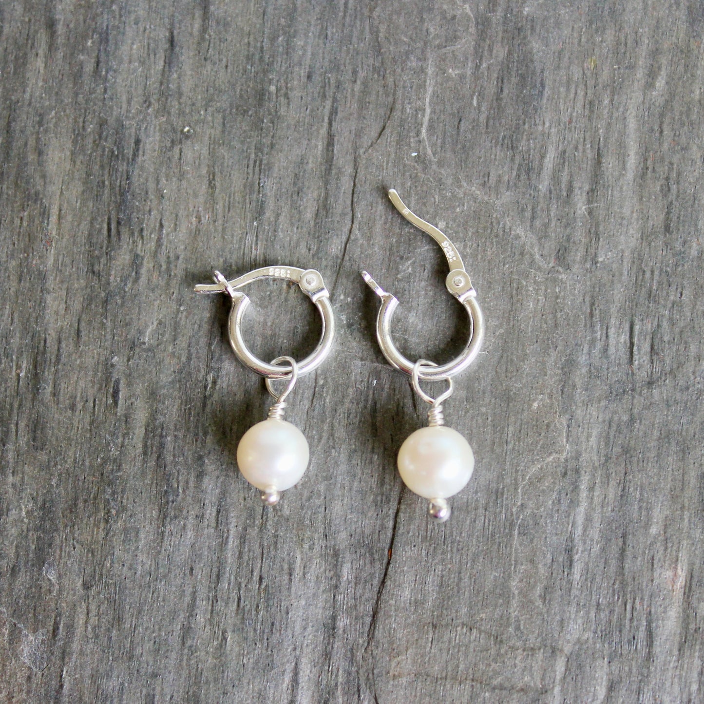Pair of silver hoop earrings with pearl drops on a wooden surface. These locking hoops are approximately 10mm in diameter with a removeable freshwater pearl drop.