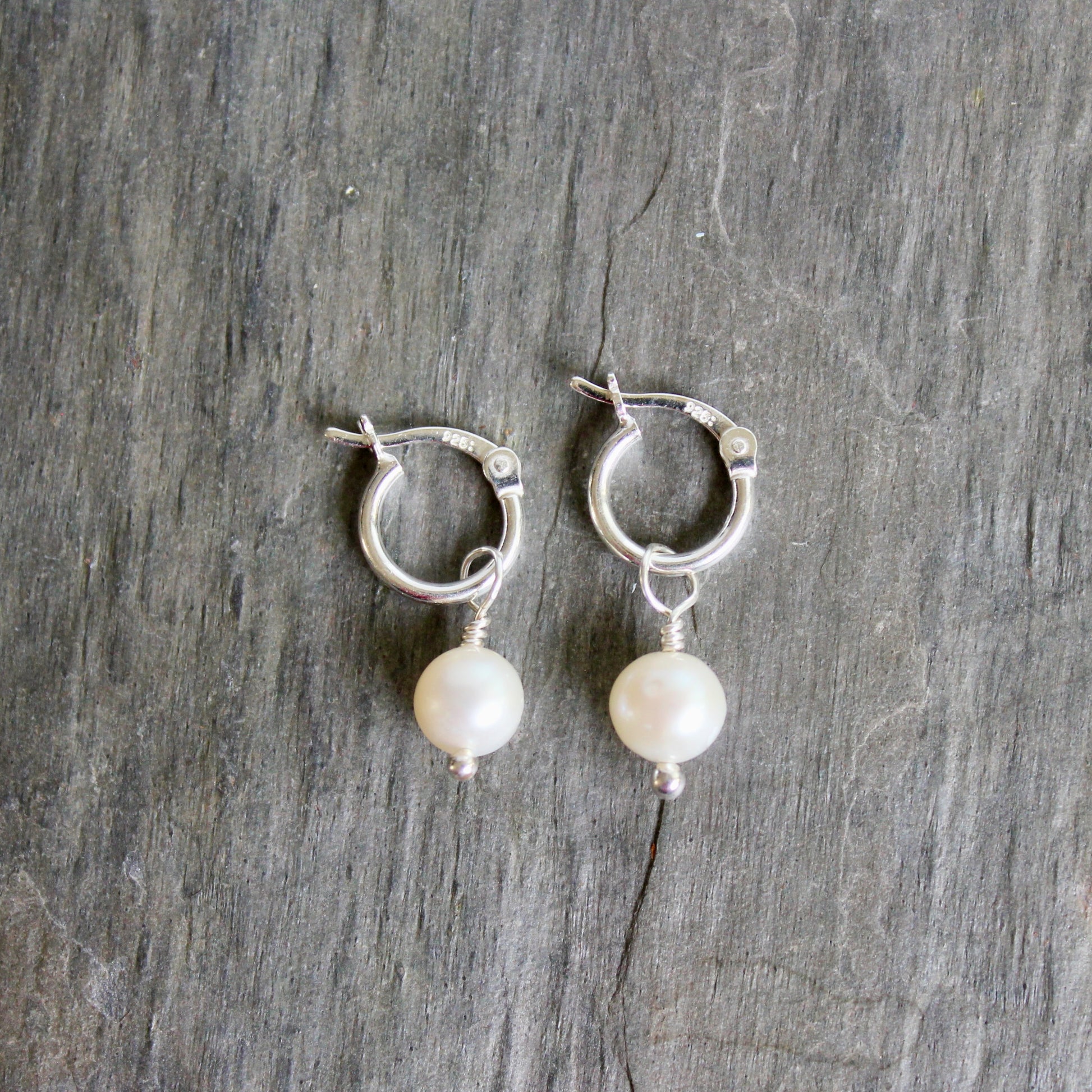 Silver hoop earrings with pearl drops on a wooden surface. These locking hoops are approximately 10mm in diameter with a removeable freshwater pearl drop.