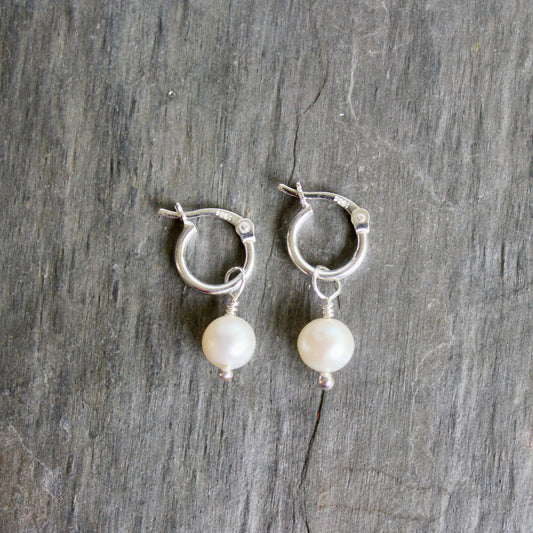 Silver hoop earrings with pearl drops on a wooden surface. These locking hoops are approximately 10mm in diameter with a removeable freshwater pearl drop.