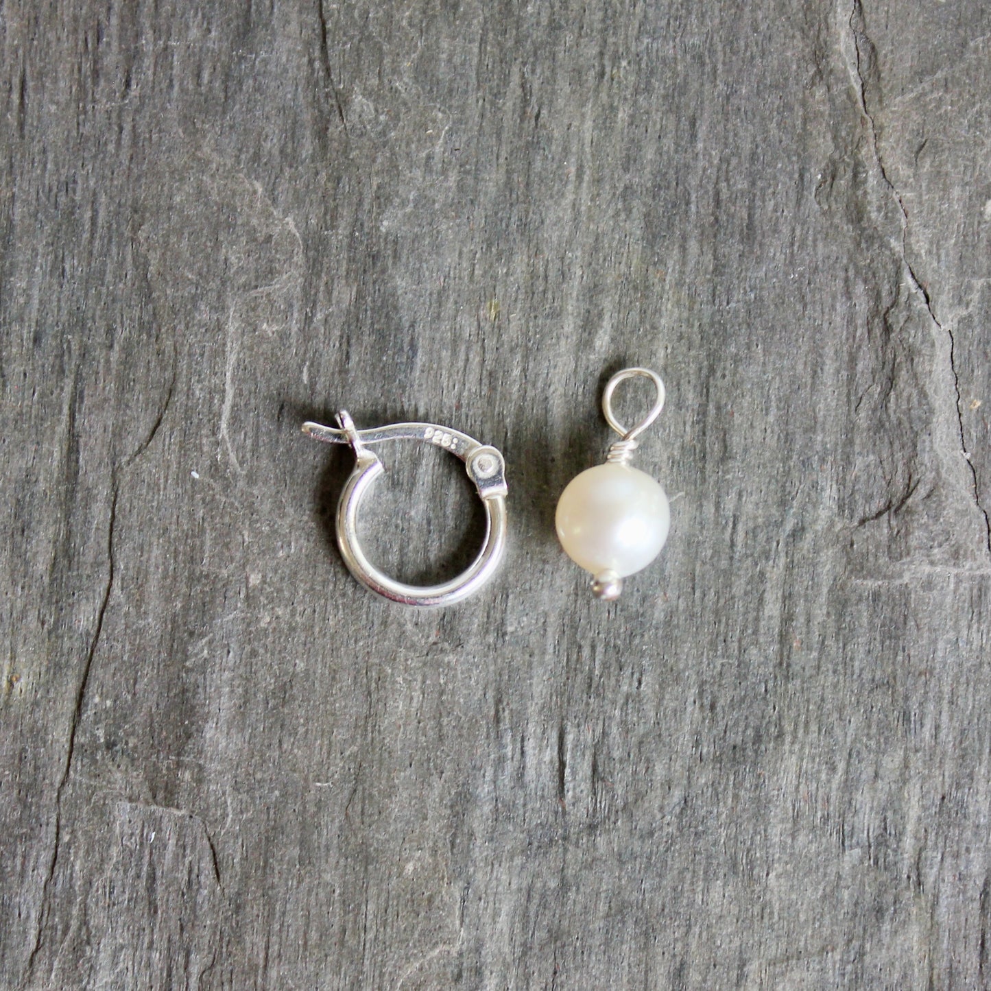 Silver ring with a pearl on a gray stone surface. These locking hoops are approximately 10mm in diameter with a removable freshwater pearl drop.