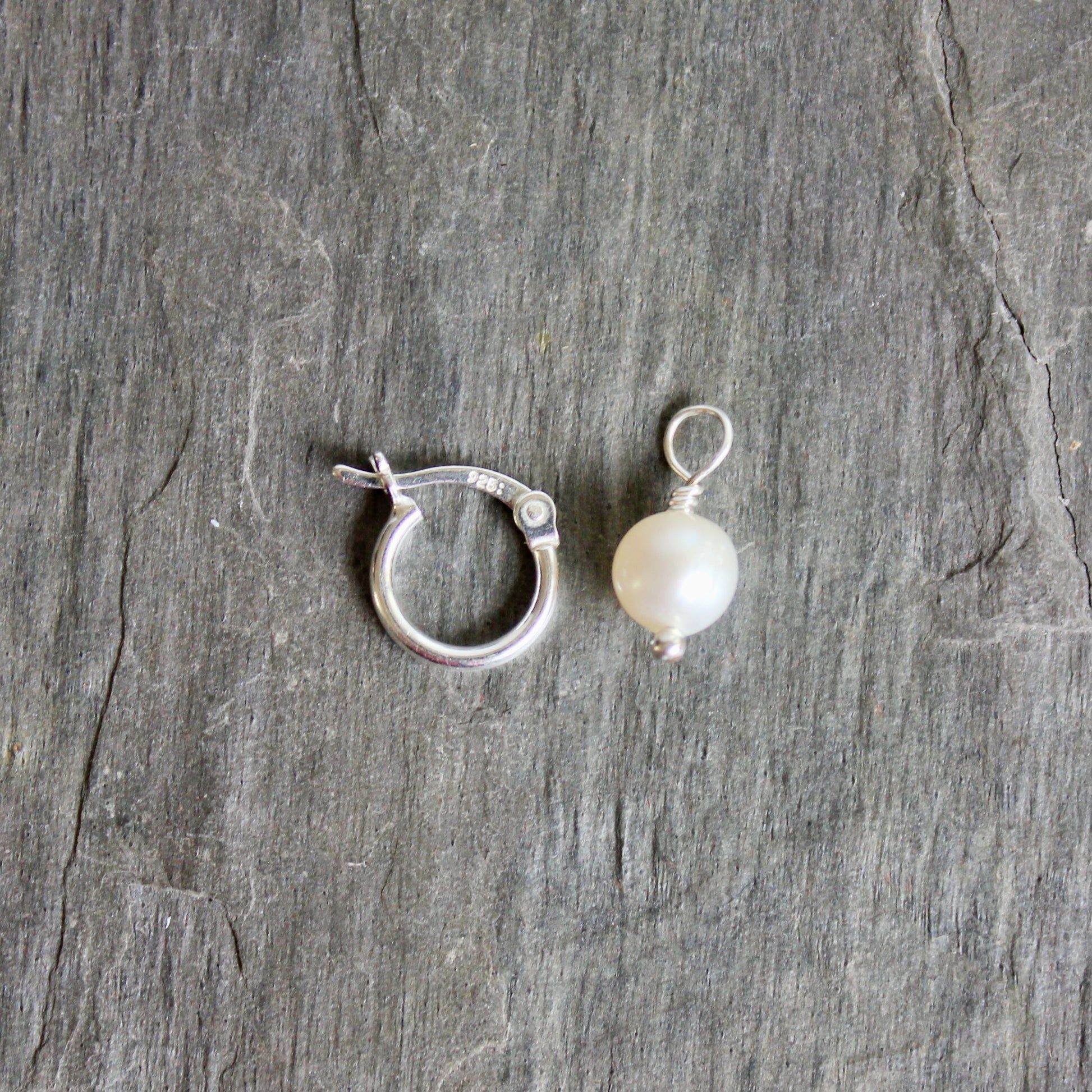 Silver ring with a pearl on a gray stone surface. These locking hoops are approximately 10mm in diameter with a removable freshwater pearl drop.